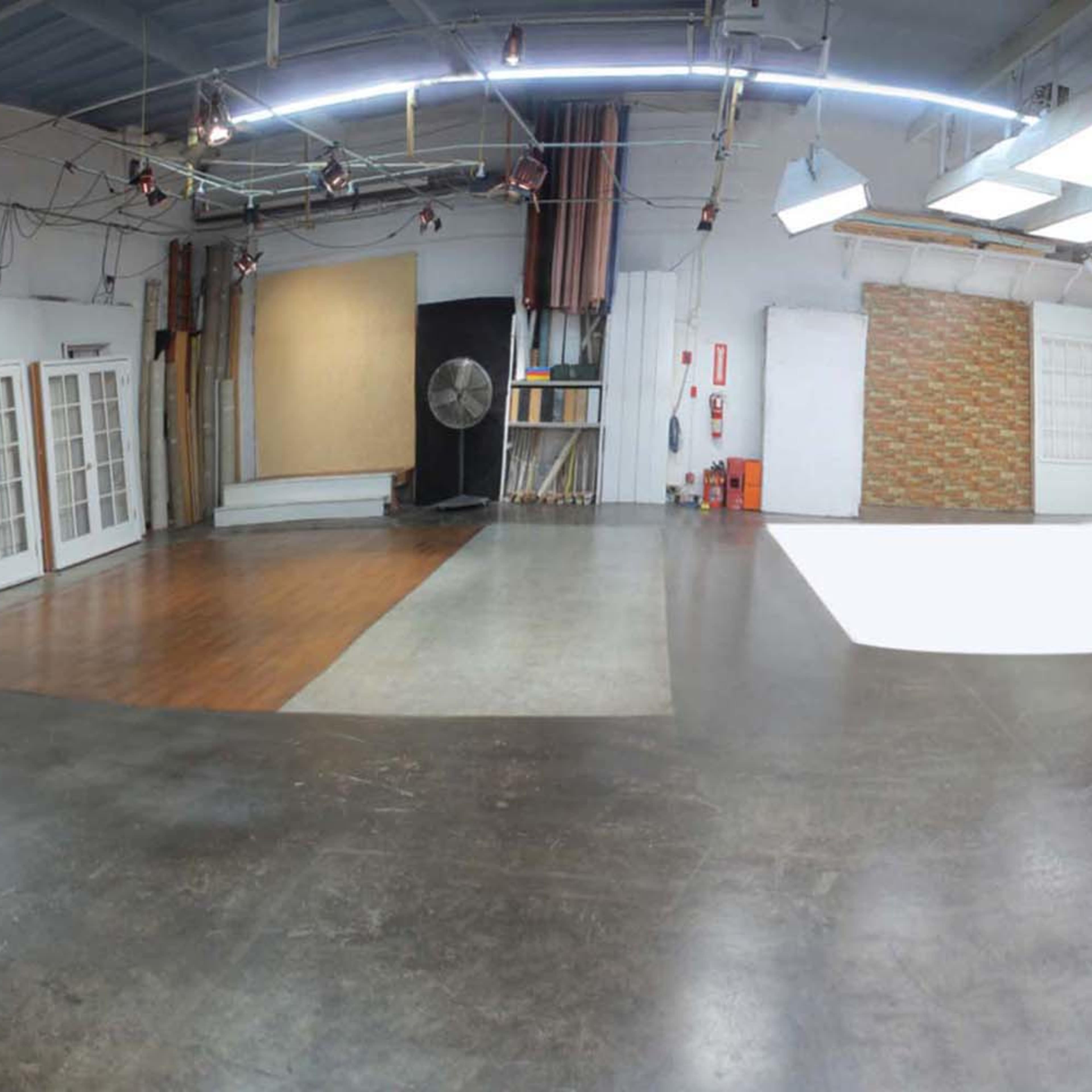 A spacious photography studio featuring a white backdrop, wooden flooring, and various lighting setups.