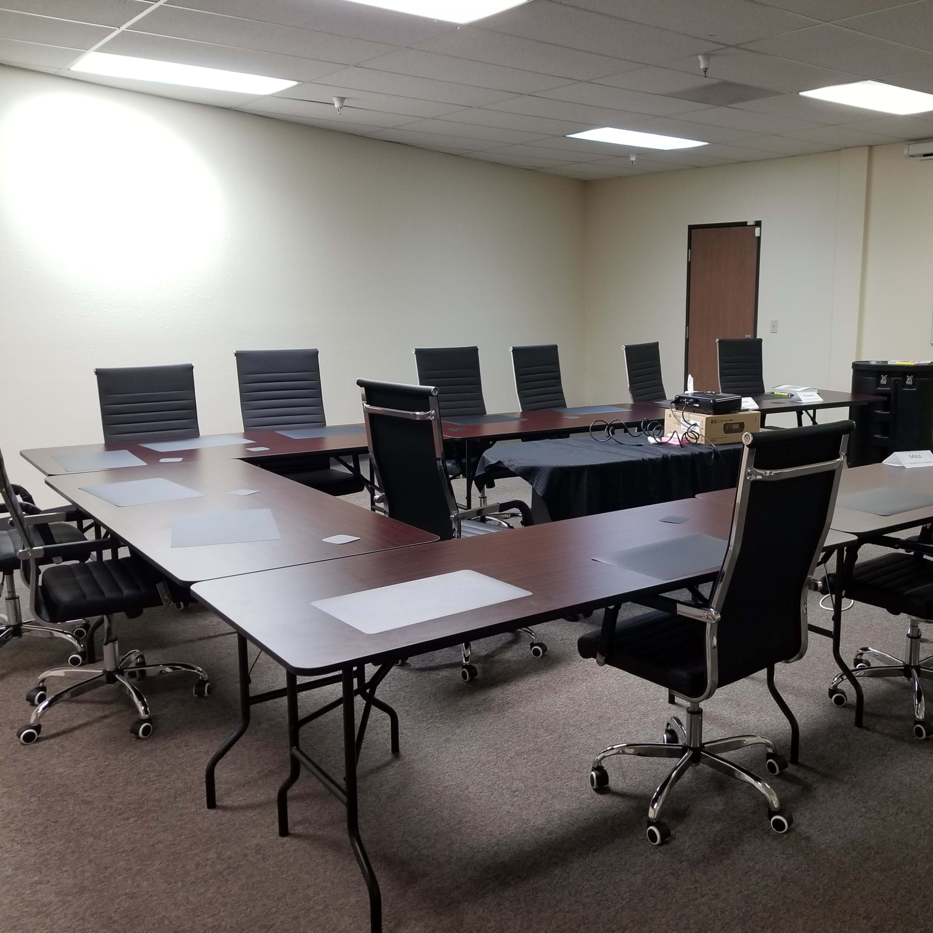 A large conference room features a long table surrounded by black chairs, with a whiteboard covered in notes on one wall.