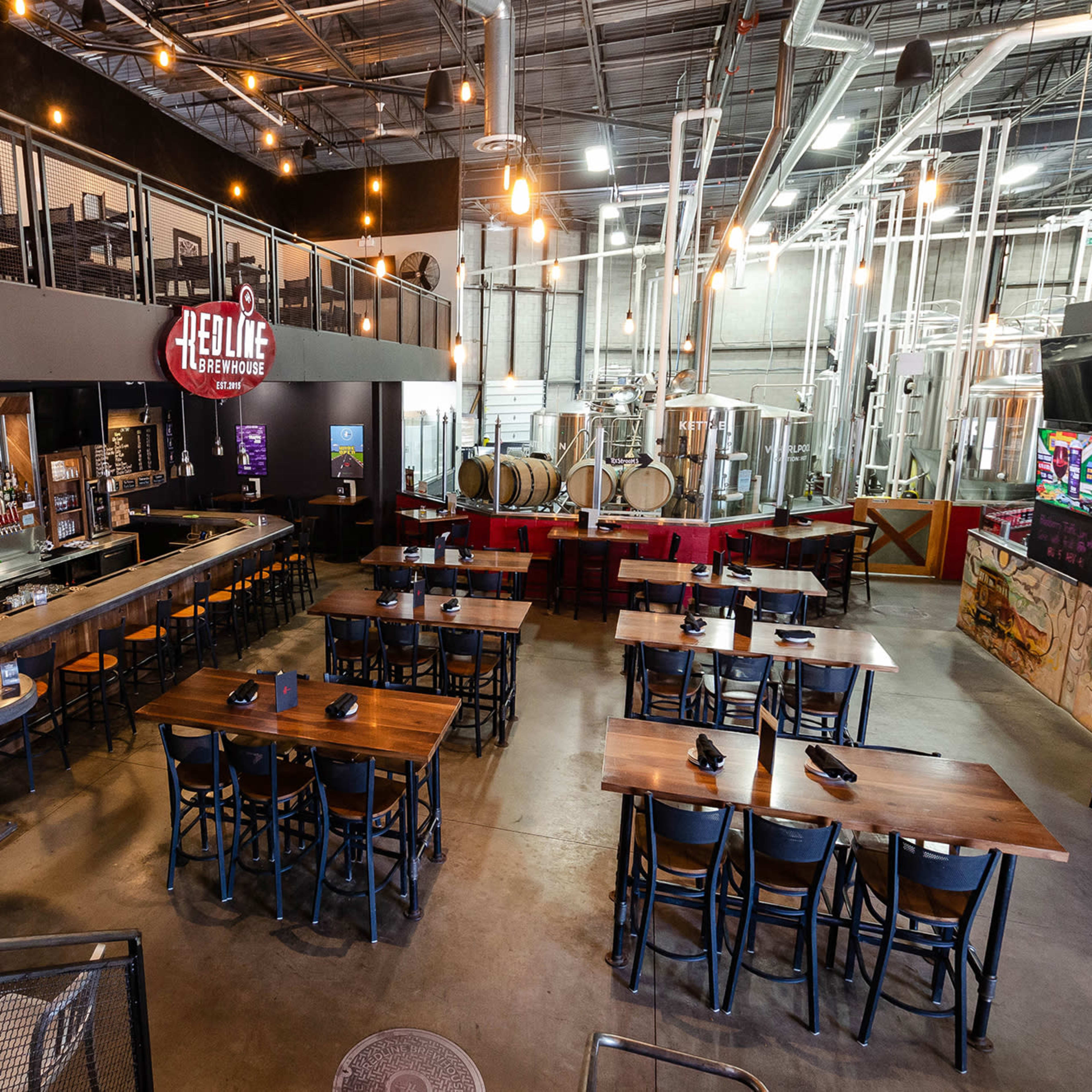 An interior view of a restaurant with a bar area, dining tables arranged in rows, and visible brewing equipment in the background.