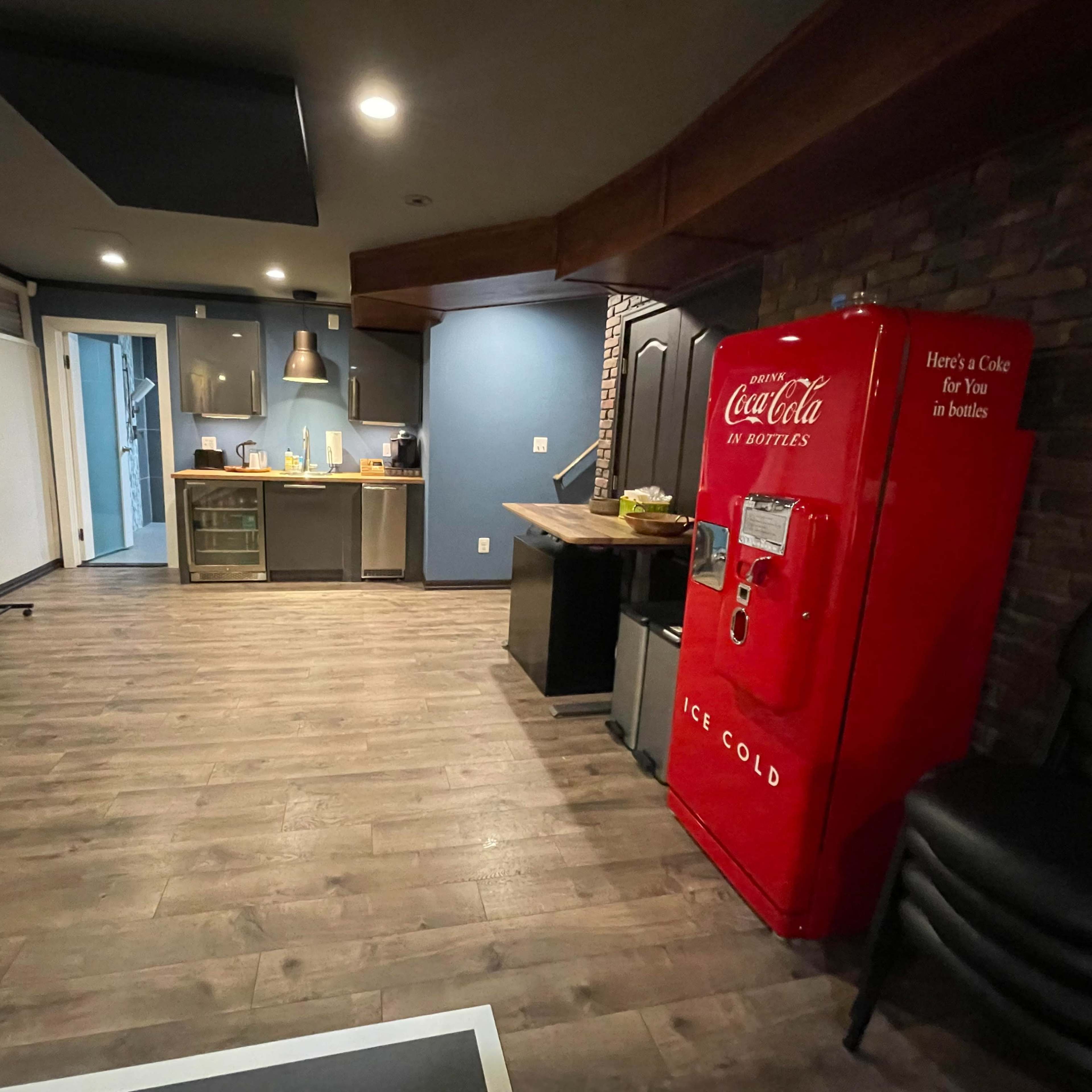 A modern kitchen space featuring a red Coca-Cola vintage refrigerator, wooden flooring, and a combination of blue and brick walls.