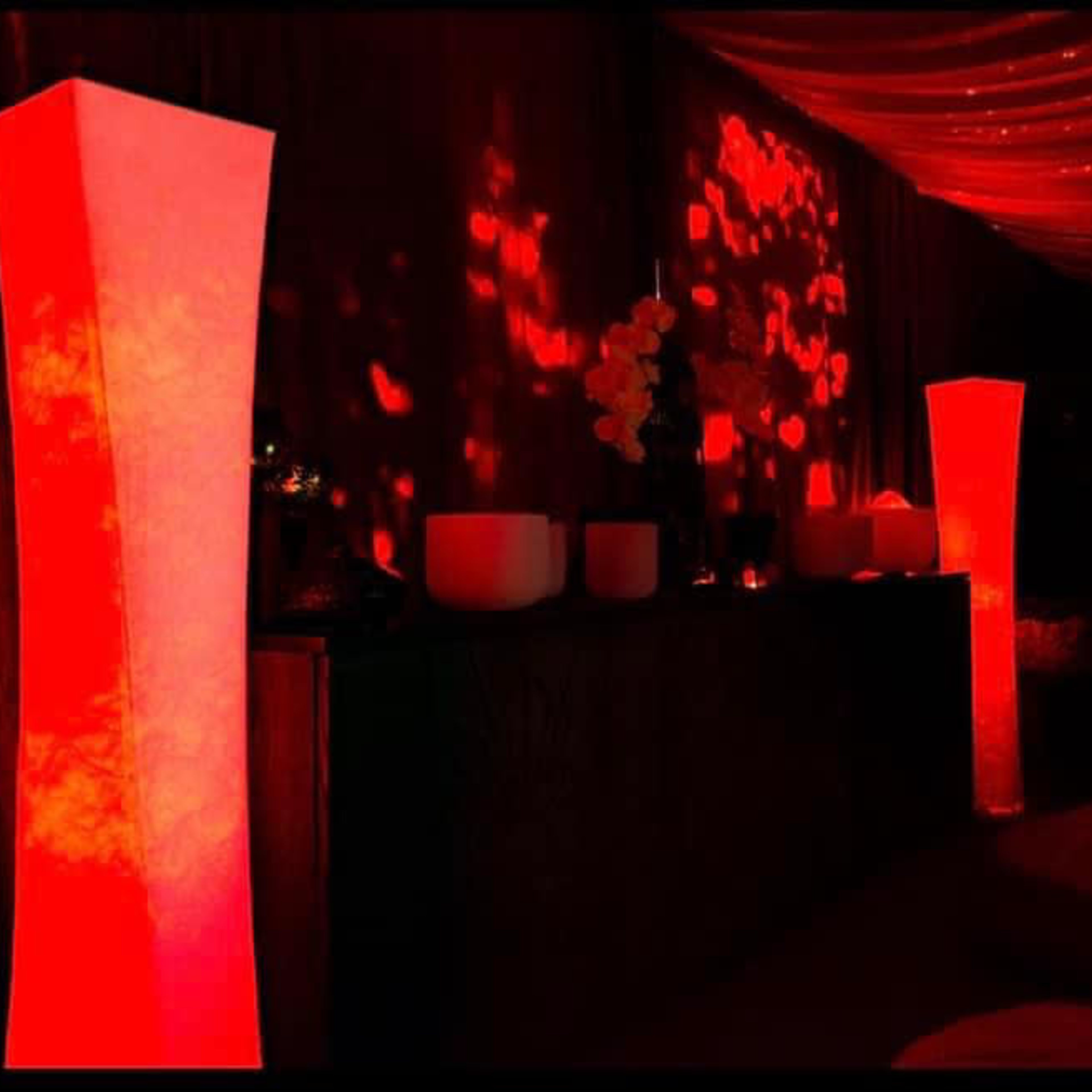 A dimly lit room with red illuminated columns, decorative candles, and soft textures in the background.