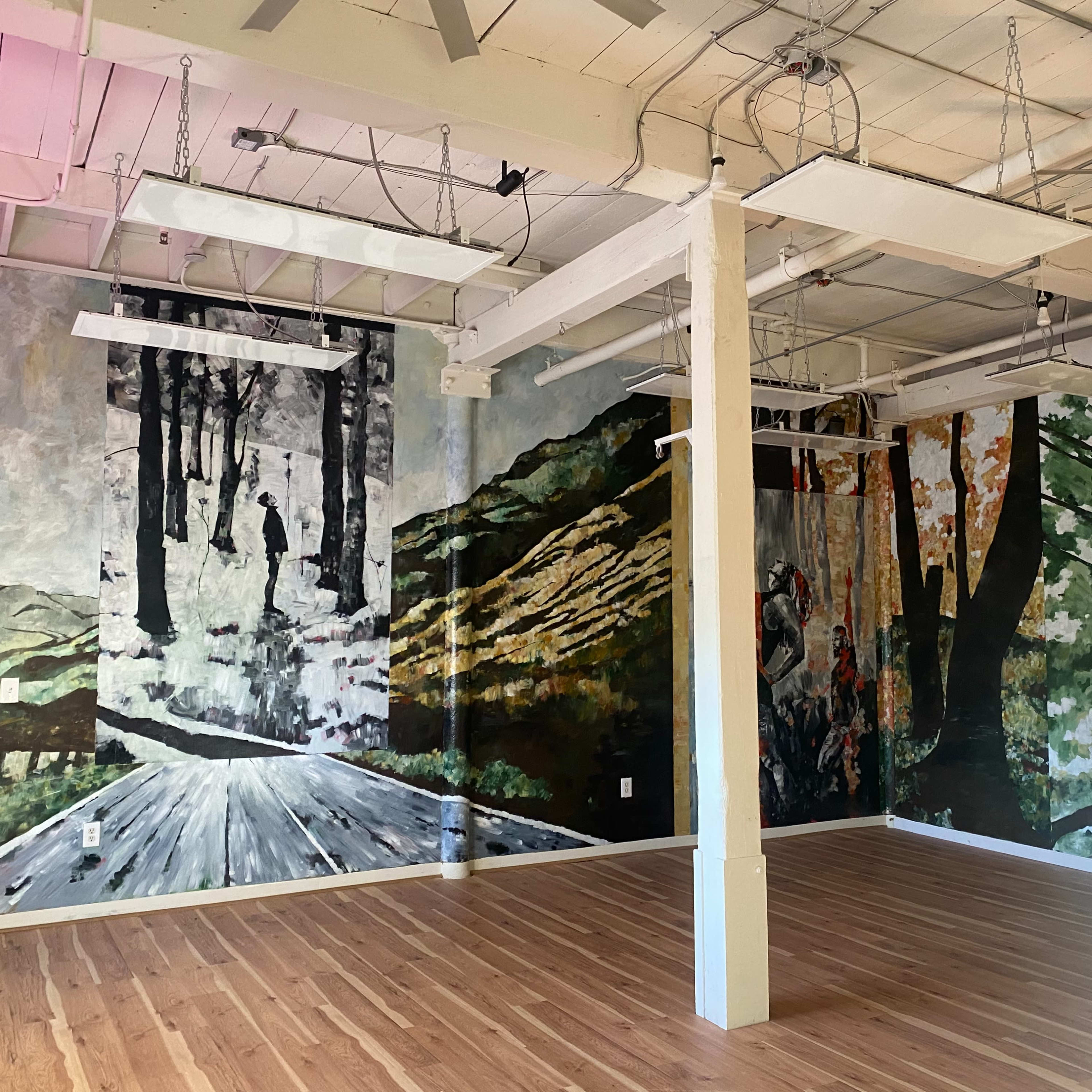 A spacious room with wood flooring and large murals depicting forested landscapes on the walls.