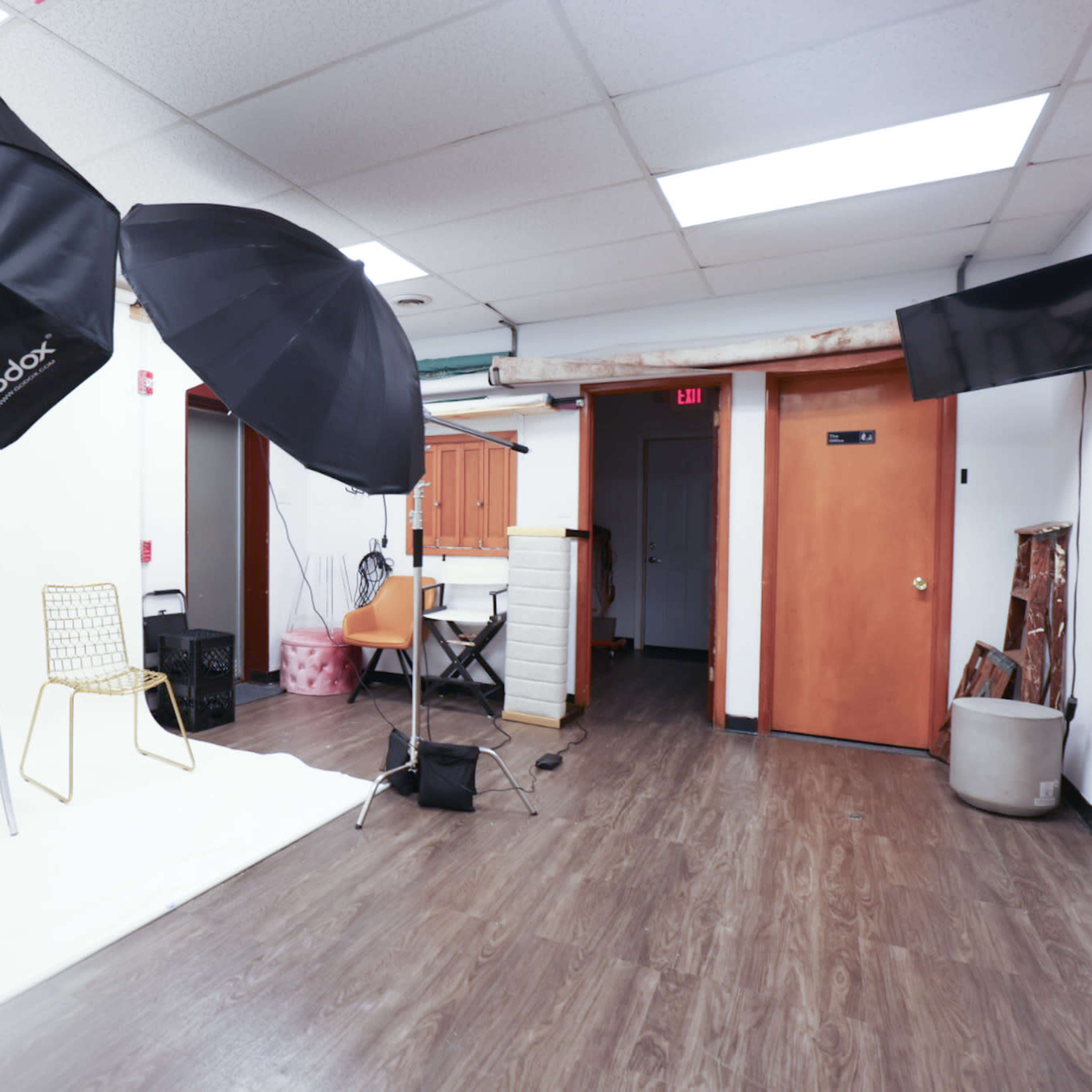 A photography studio with lighting equipment, a white backdrop, and a few chairs arranged in the space.