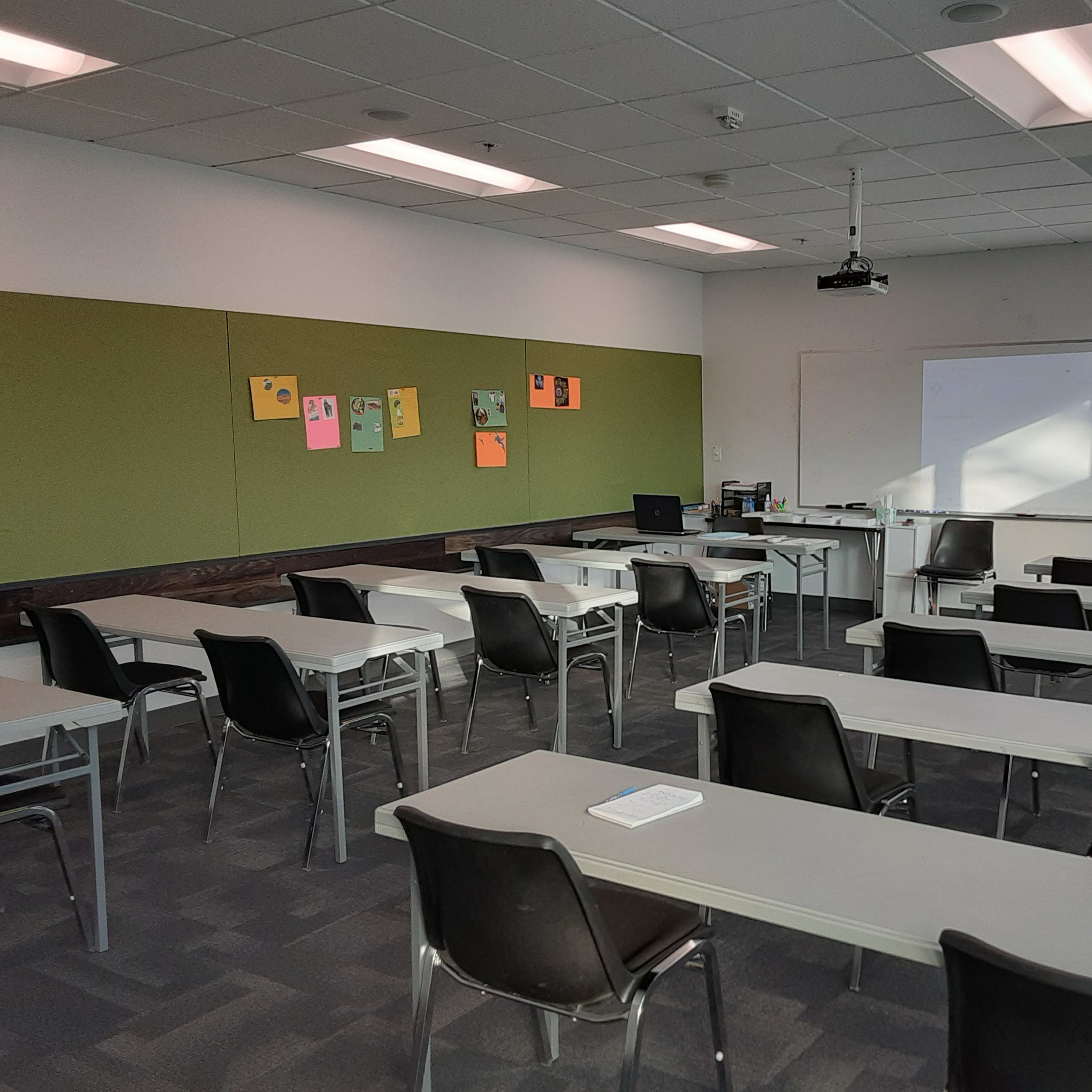 A classroom with rows of desks and chairs facing a whiteboard at the front, along with colorful papers mounted on the walls.