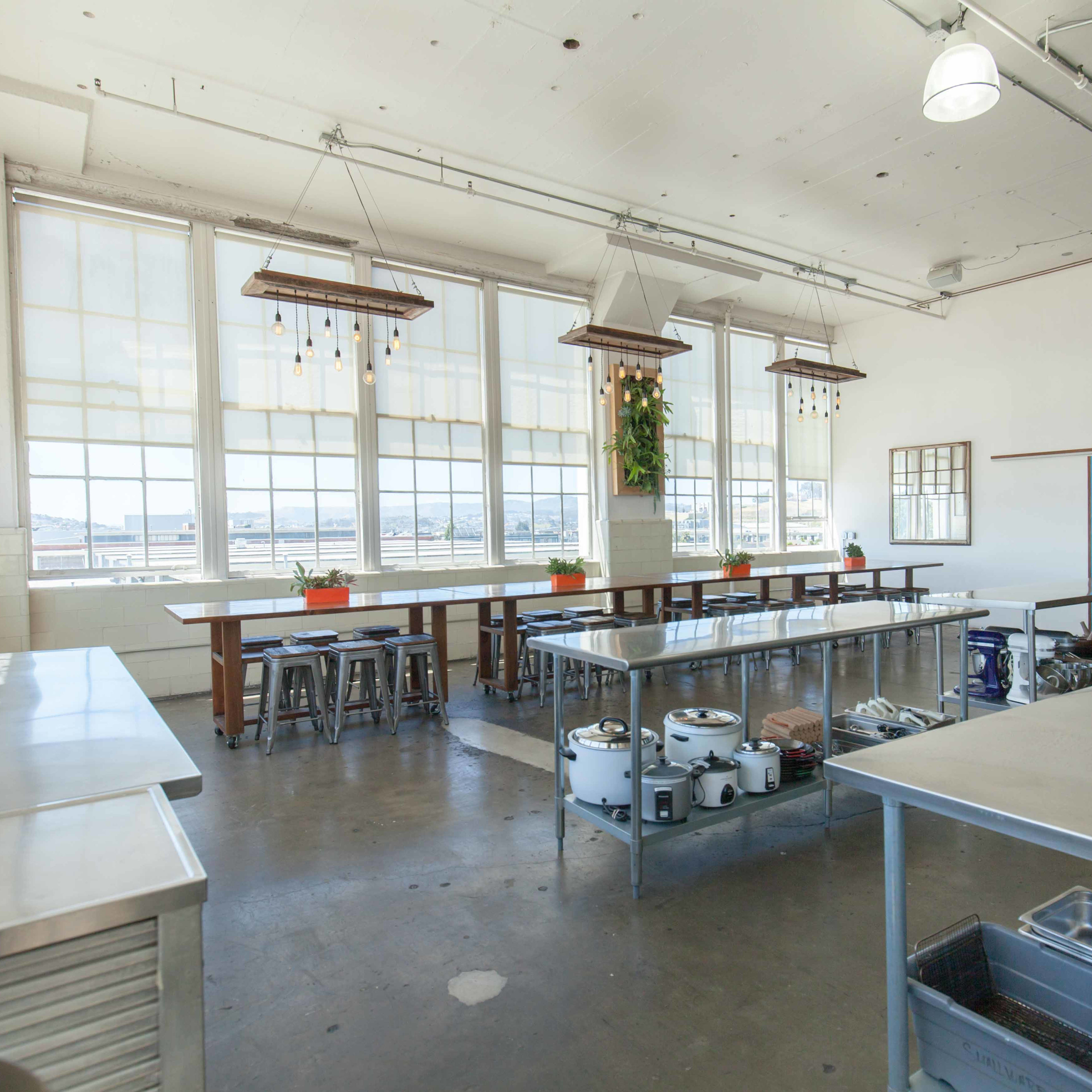 A spacious kitchen with large windows, stainless steel worktables, and overhead lighting.
