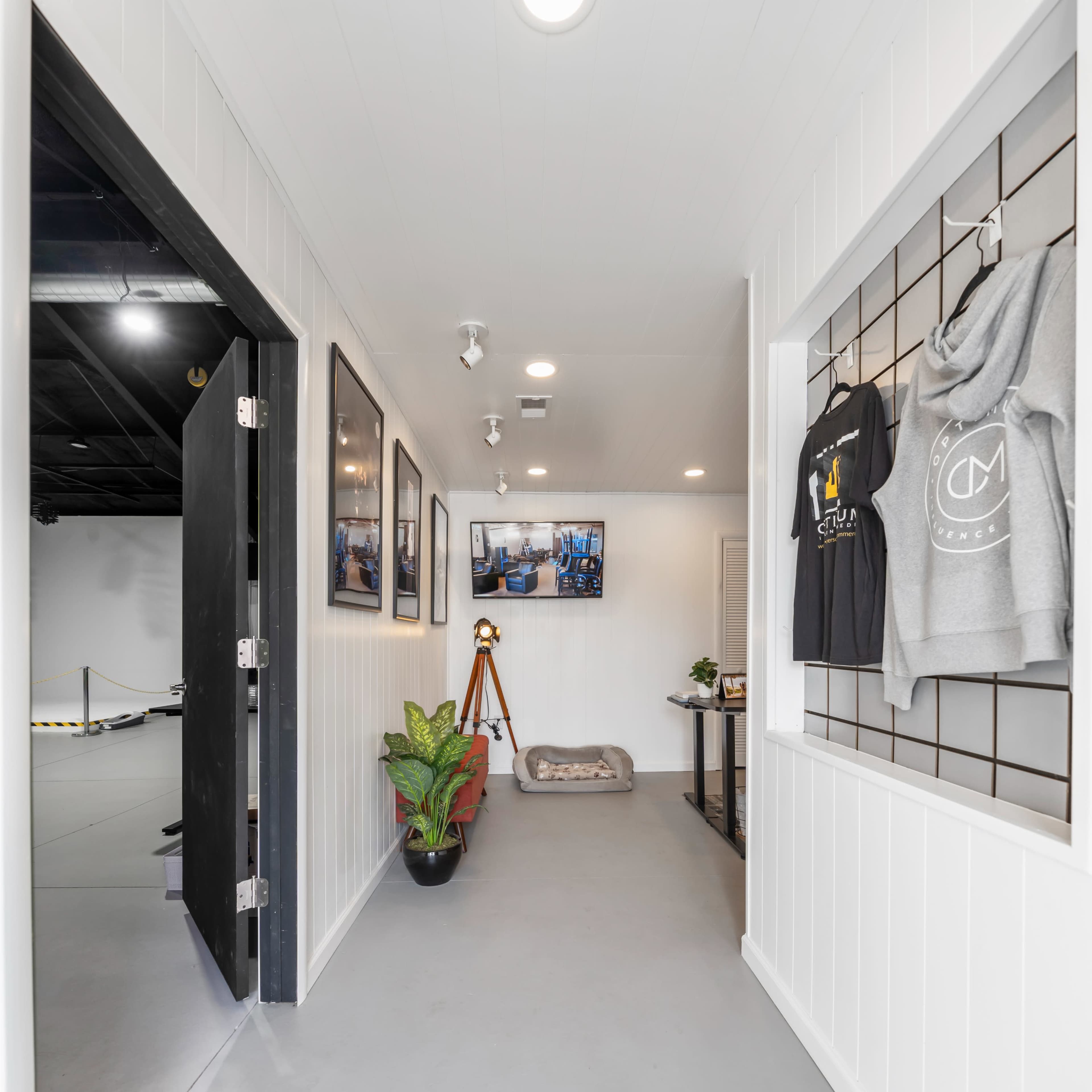 A narrow hallway leading to a bright, minimalist space featuring clothing displays, artwork on the walls, and a small seating area.
