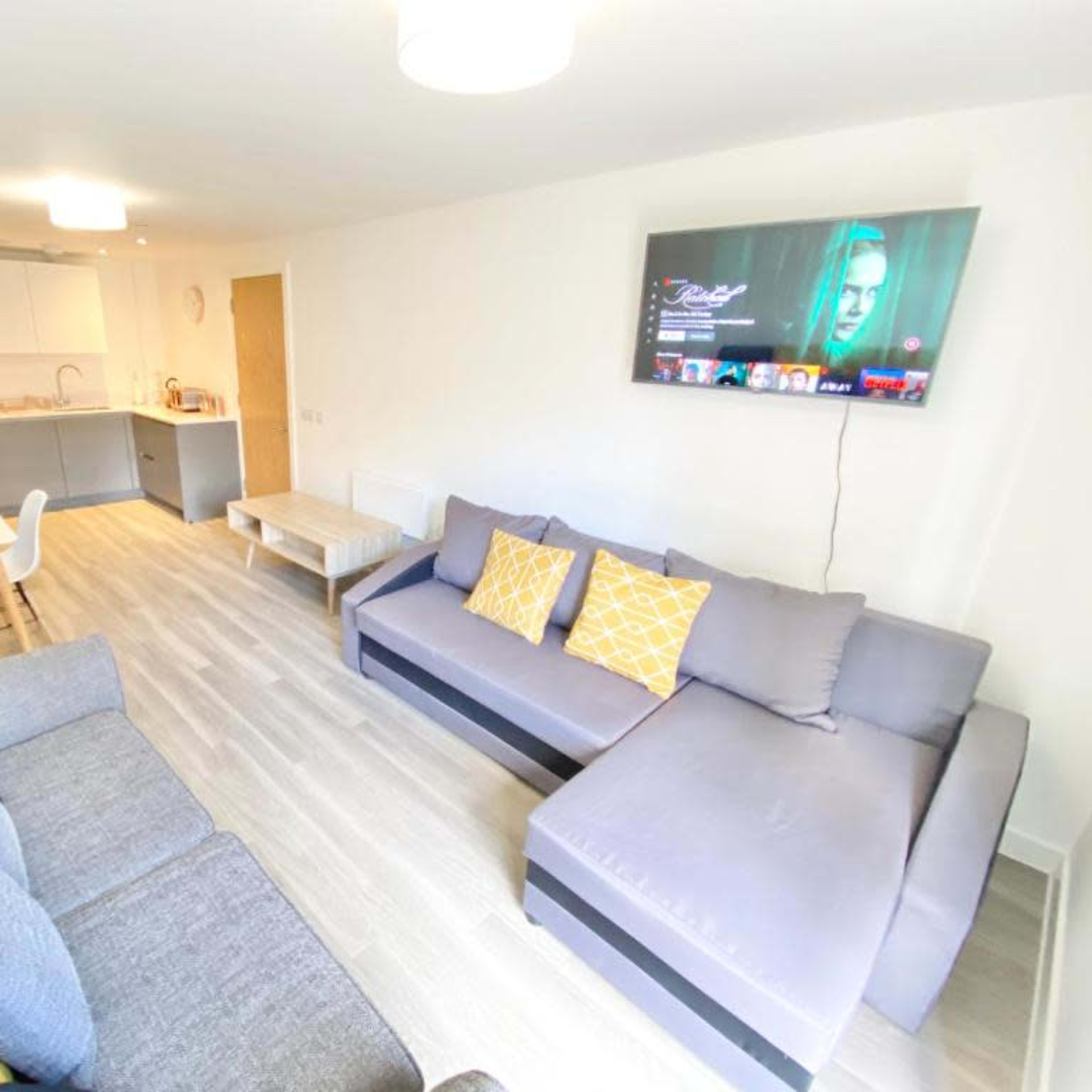 A modern living room with gray couches, a light-colored table, and a wall-mounted television.