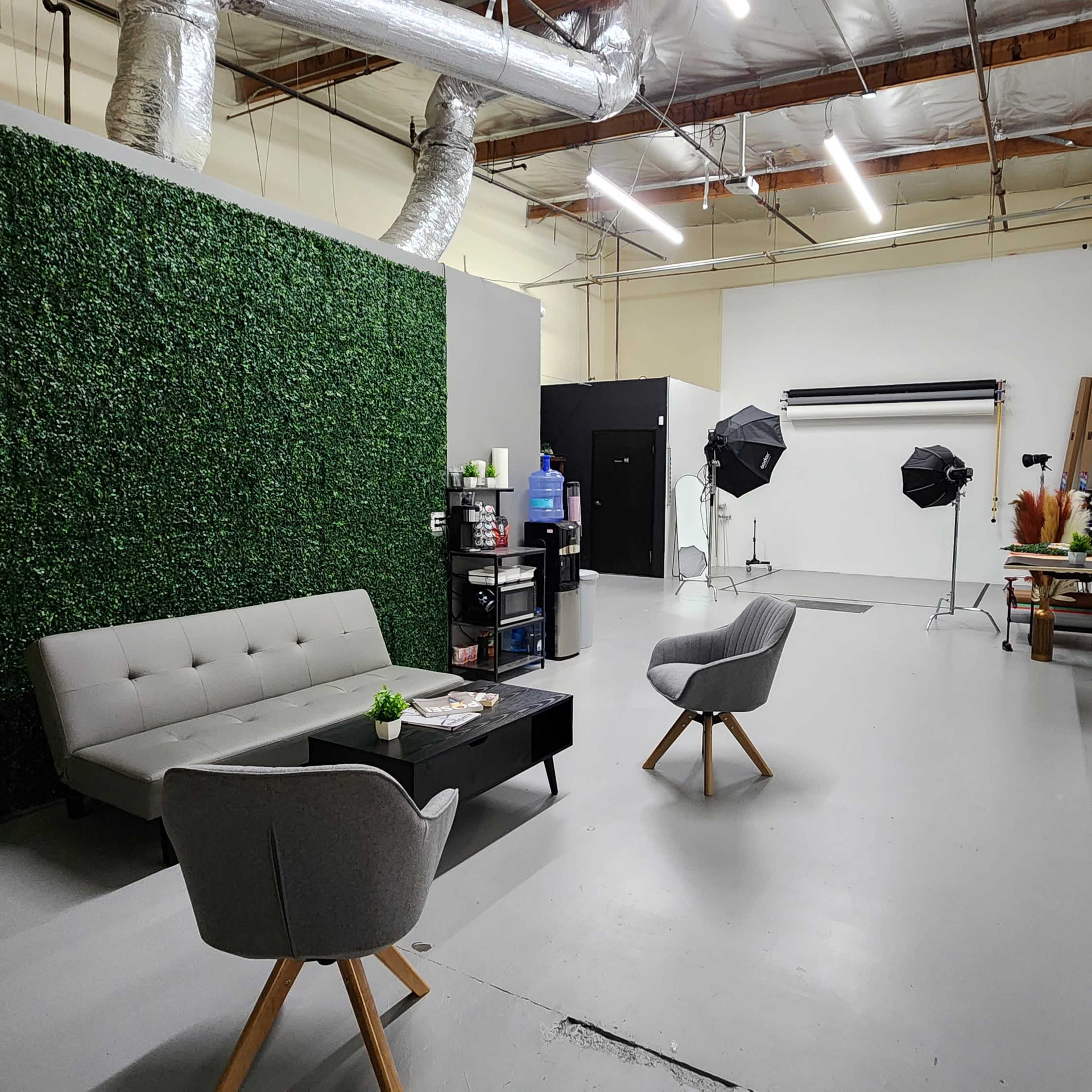 A spacious interior with a green wall, a gray sofa and chairs, and photography equipment set up in a studio environment.