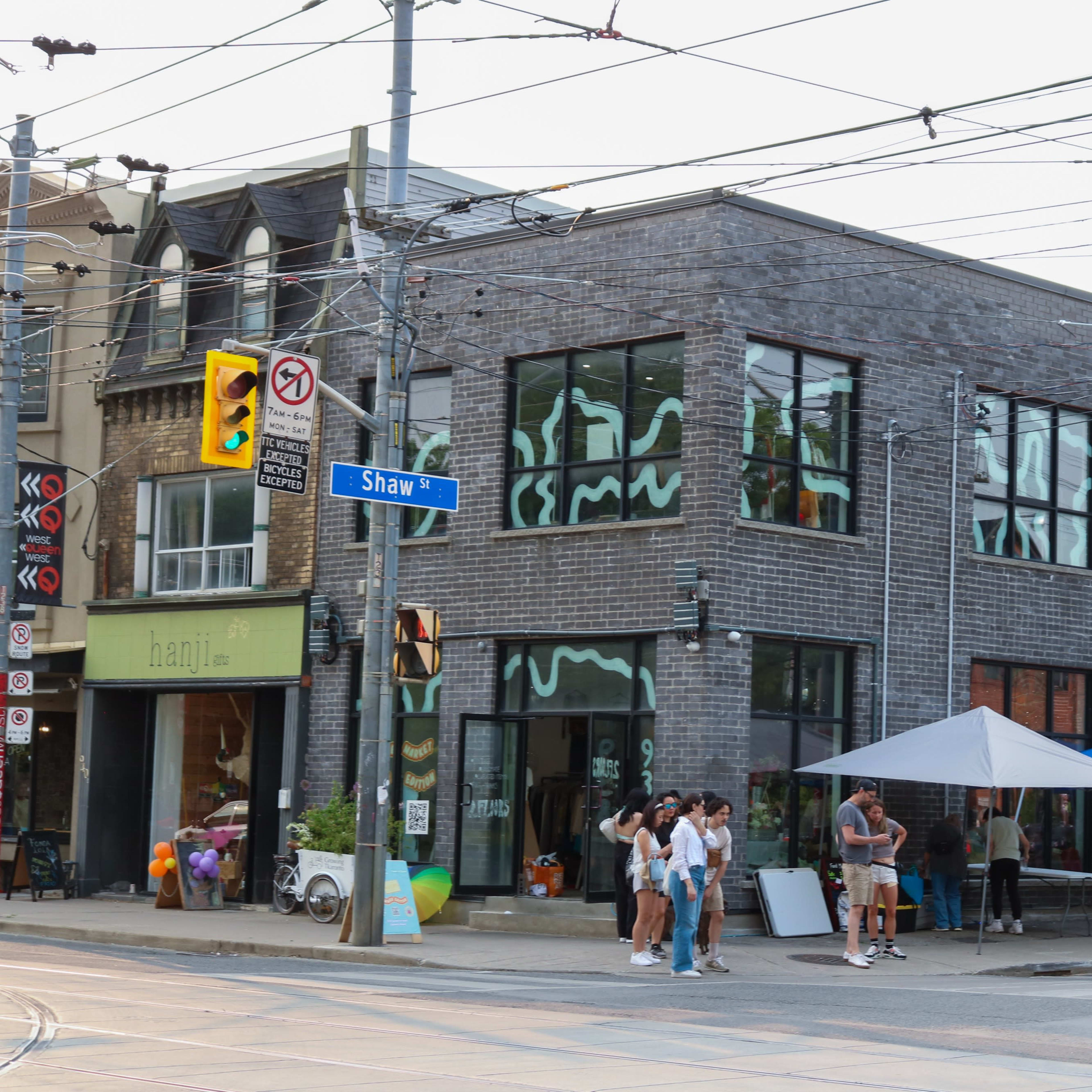 A street corner with a modern building featuring large windows and multiple vendors under blue tents selling goods.