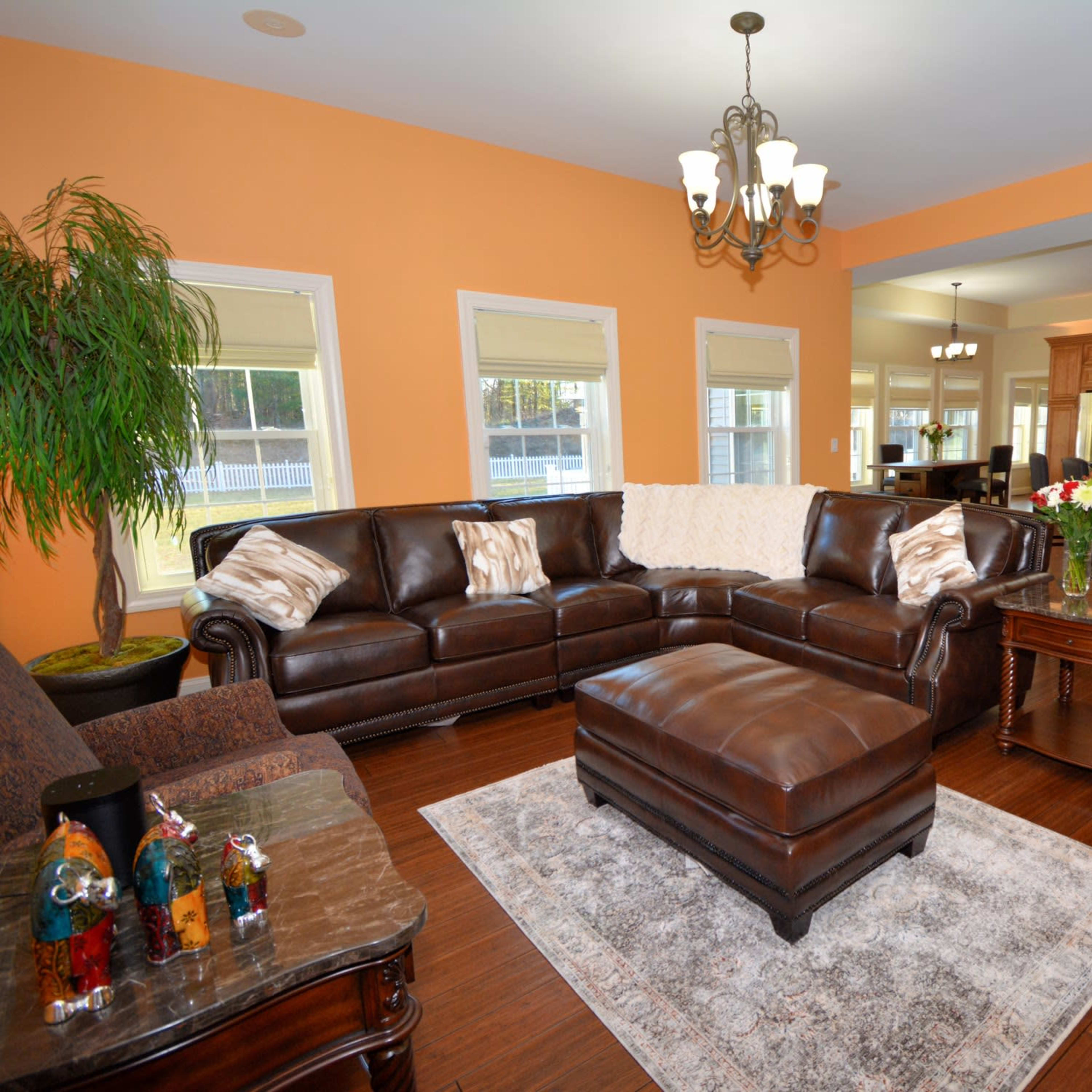 The living room features a brown leather sectional sofa, a coffee table, and a kitchen in the background with wooden cabinetry.