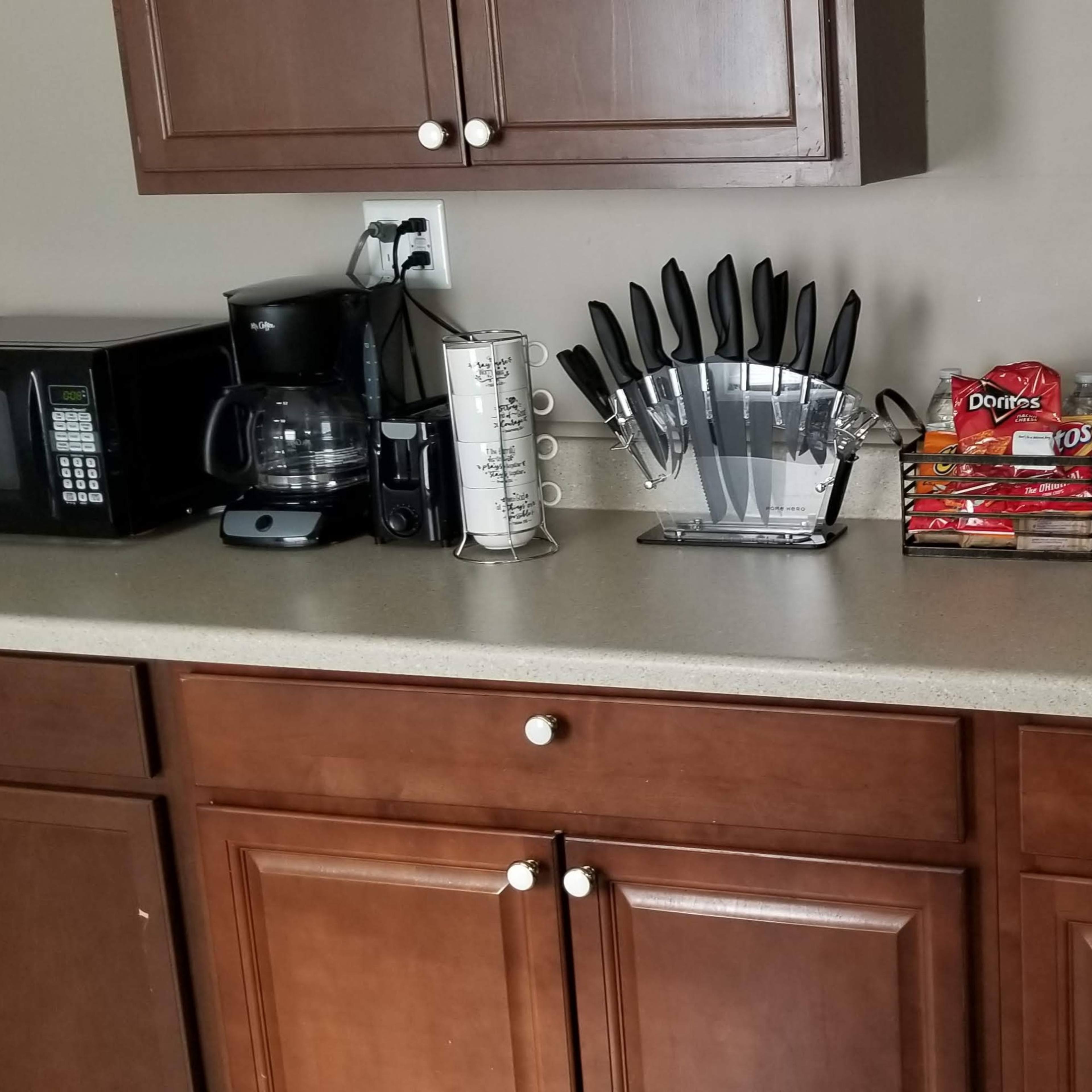 A kitchen countertop with a microwave, coffee maker, knife block, paper towels, and a sink.