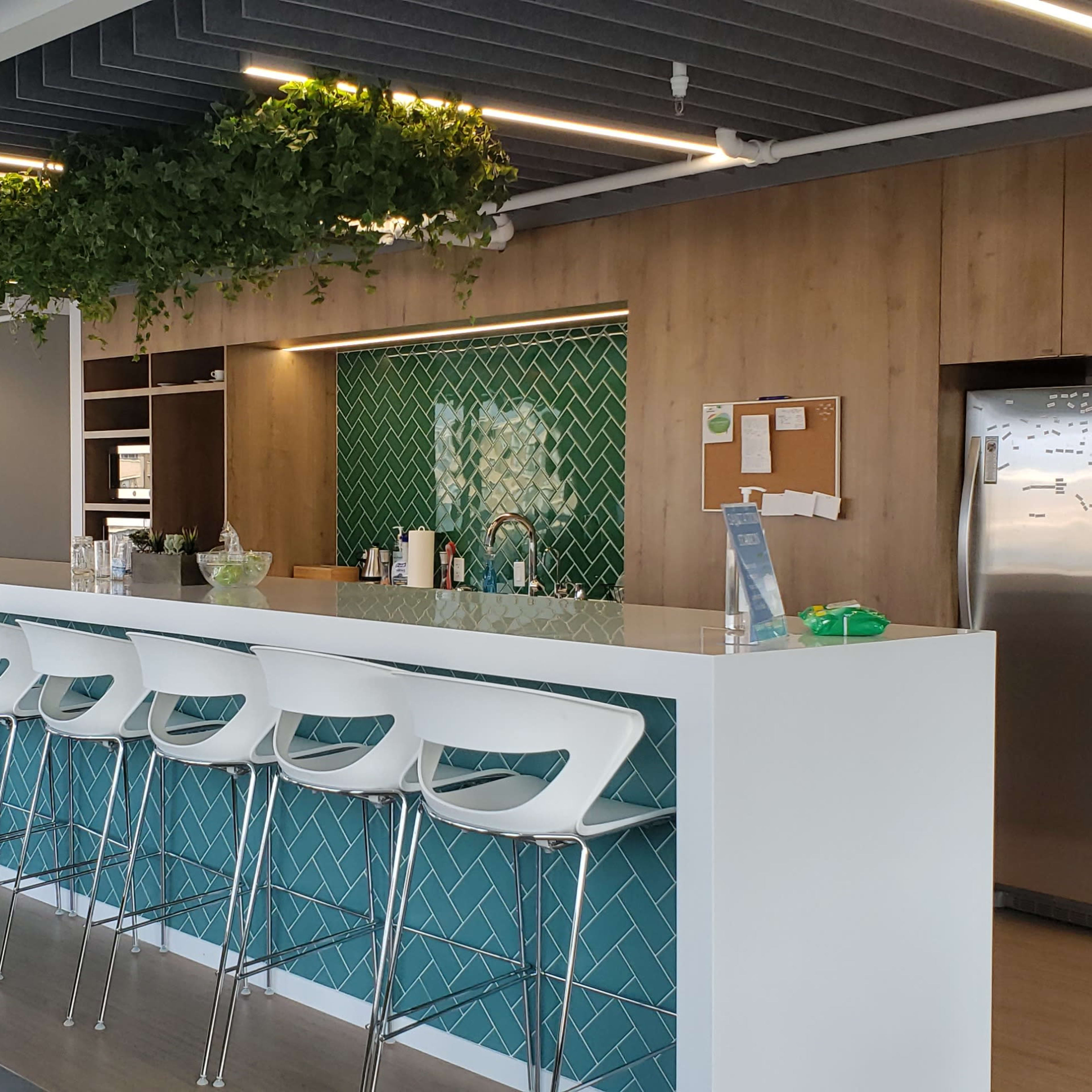 A modern kitchen area with a bar counter, high stools, and green wall decor, along with a refrigerator and a seating area in the background.