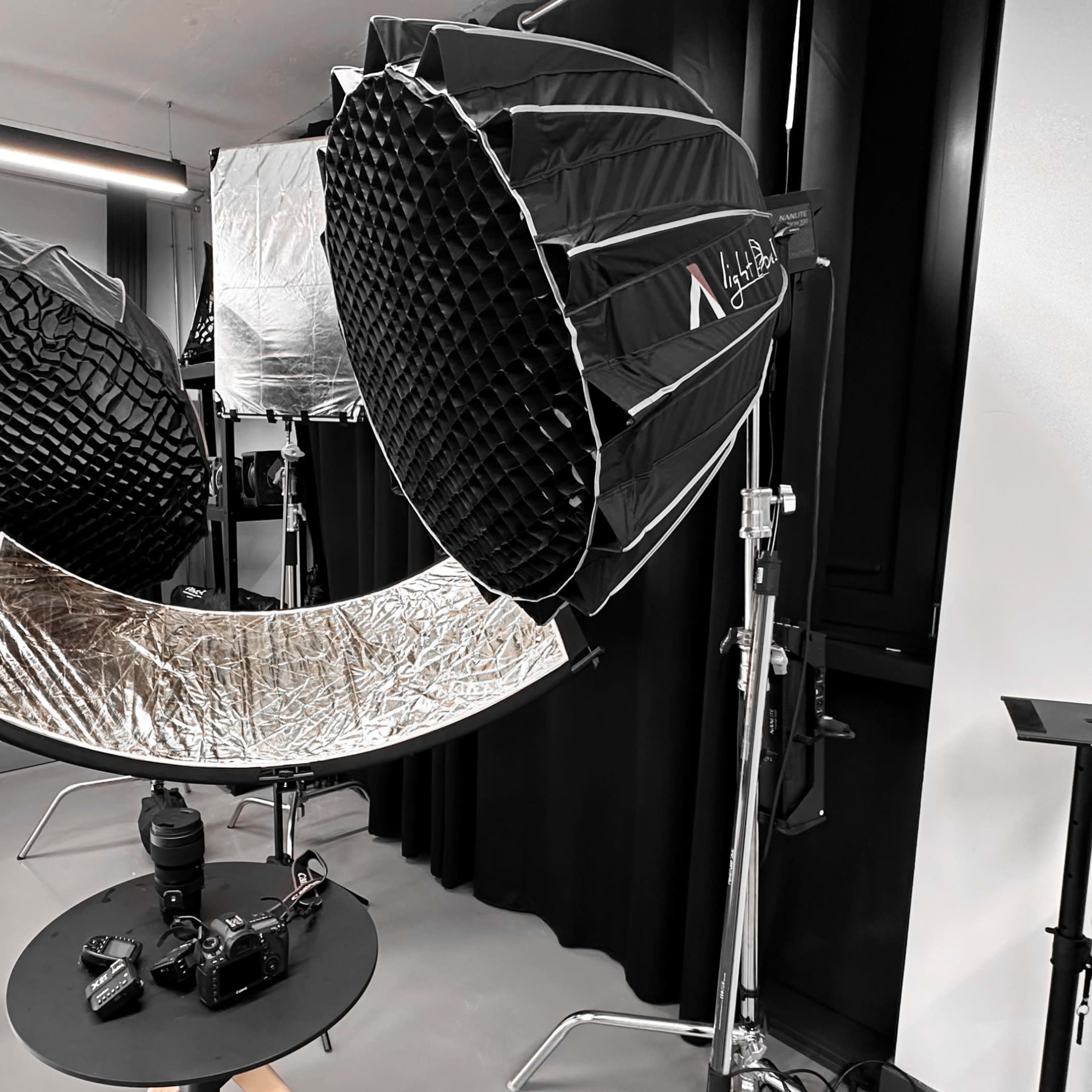 A photography setup with large softbox lights, a reflector, and a camera positioned on a table in a studio environment.