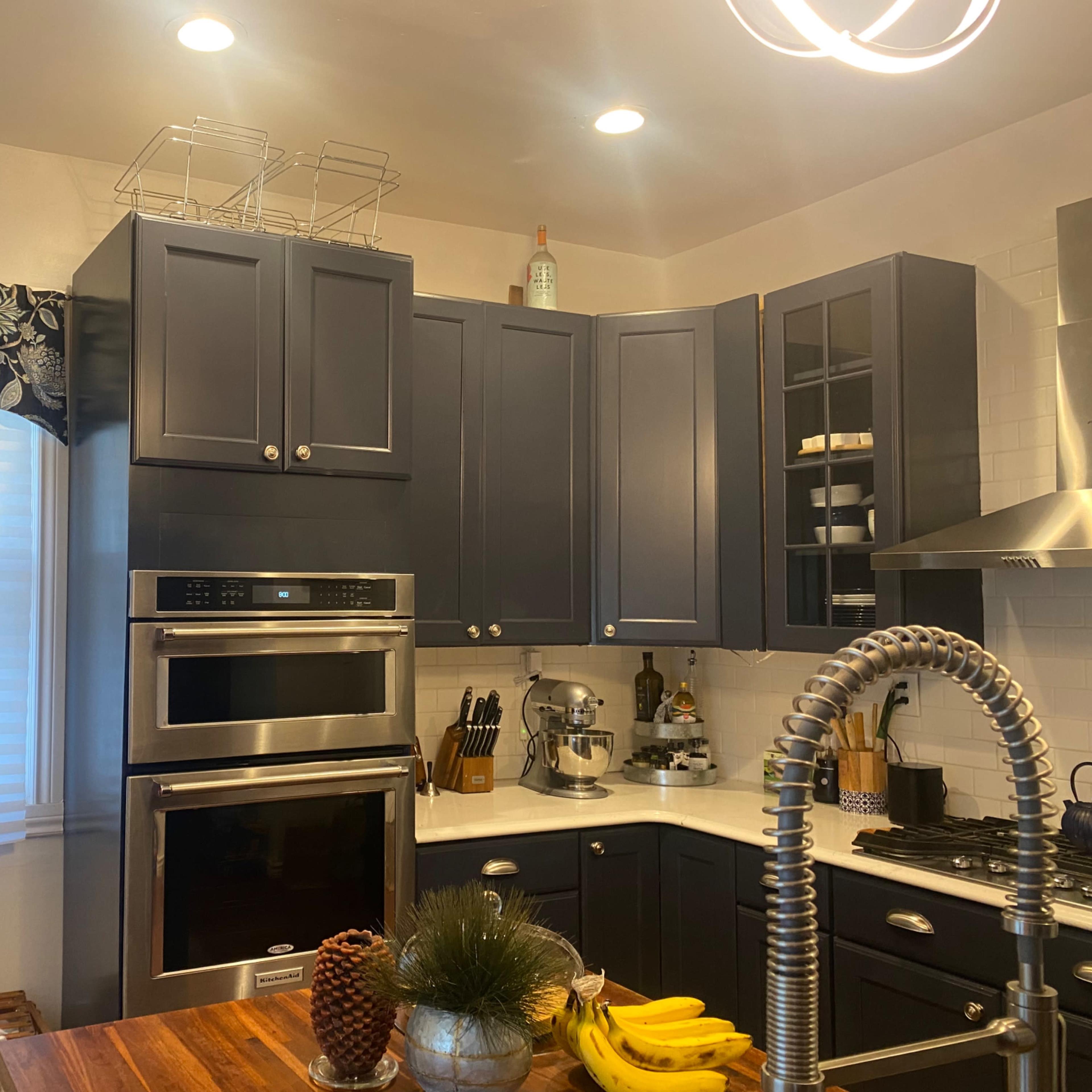 A modern kitchen with navy blue cabinets, stainless steel appliances, and a wooden countertop featuring a fruit display.