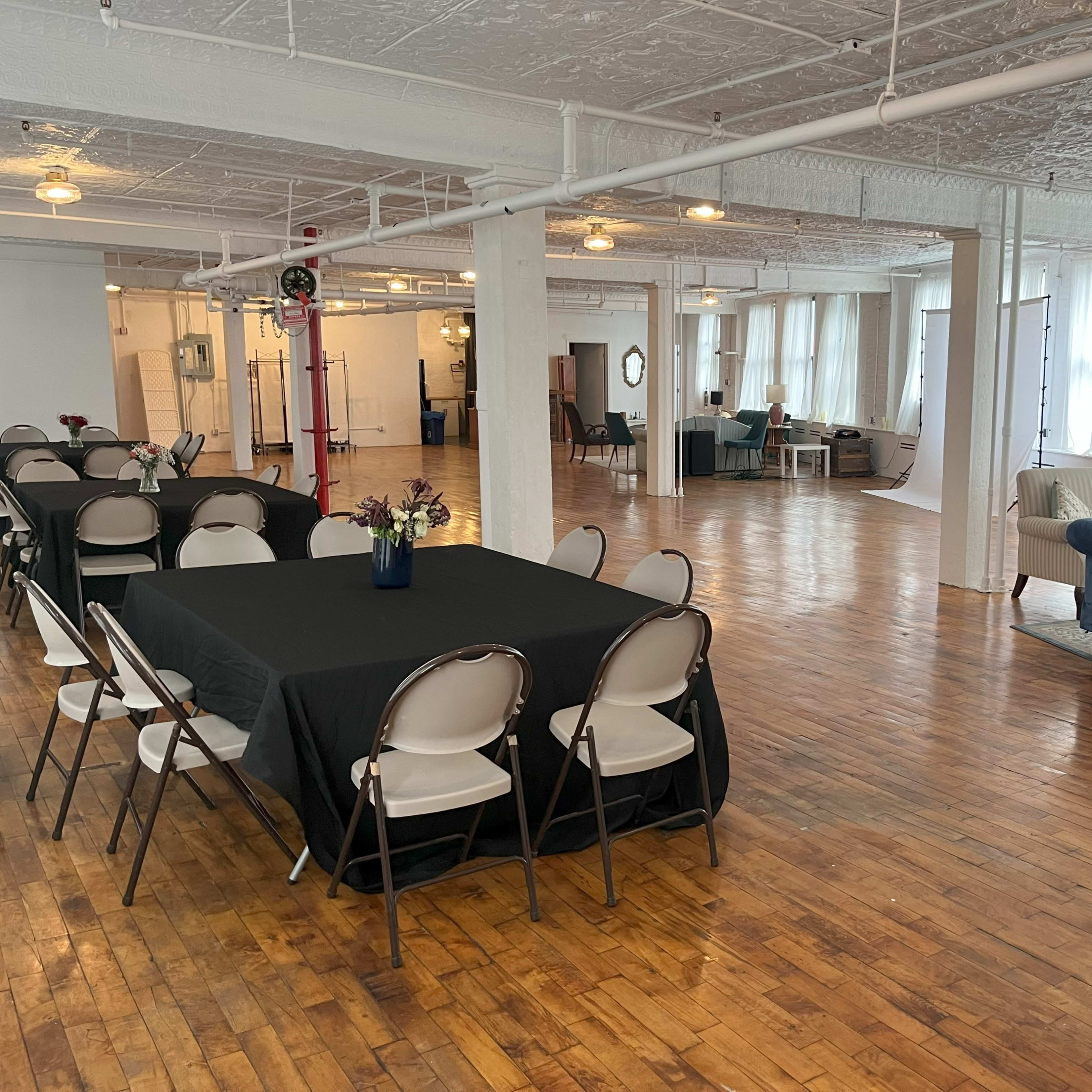 A large, airy studio space with wooden flooring, several tables set with black tablecloths, and a blue sofa in one corner.
