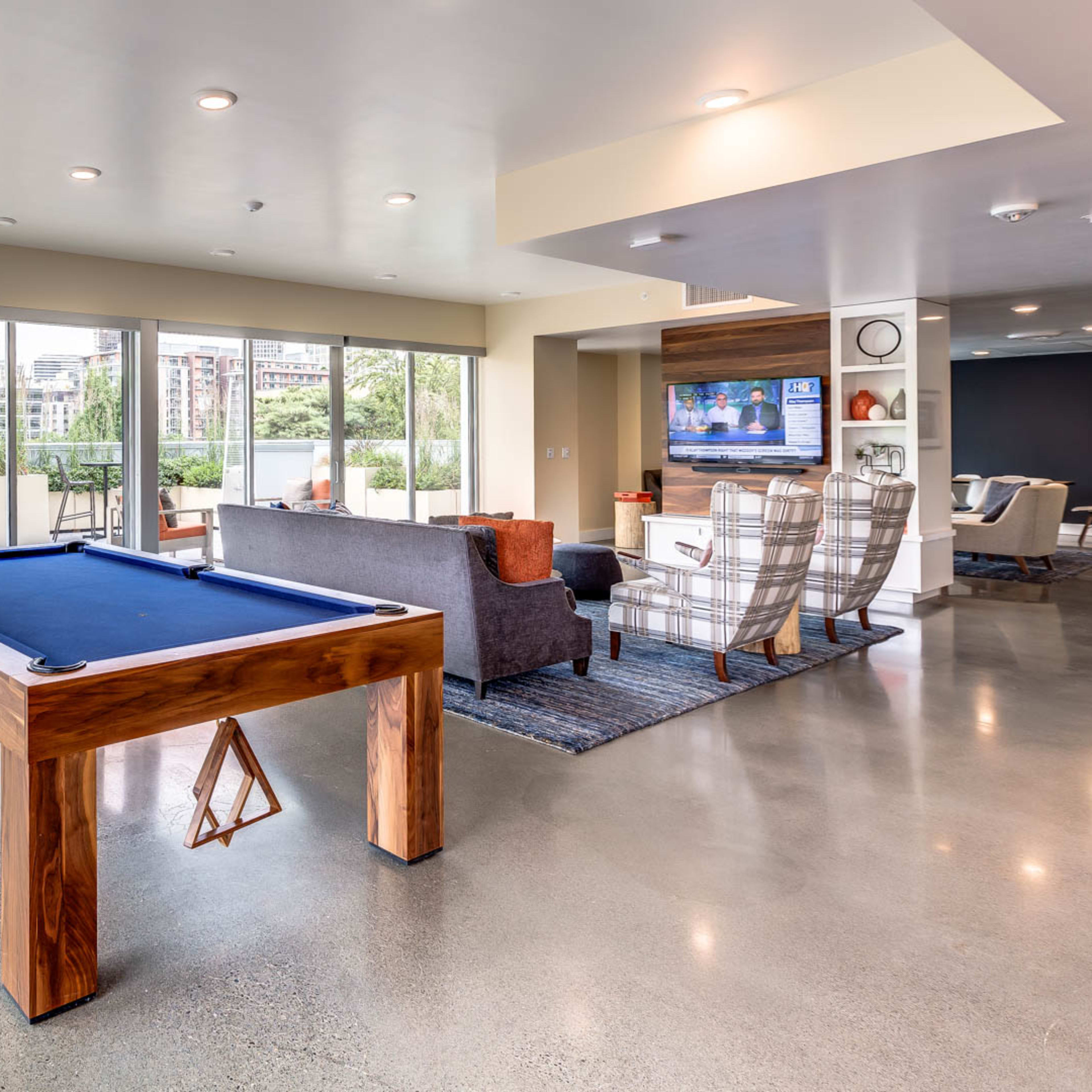 A modern indoor recreation area featuring a pool table, seating arrangements, large windows, and a television.