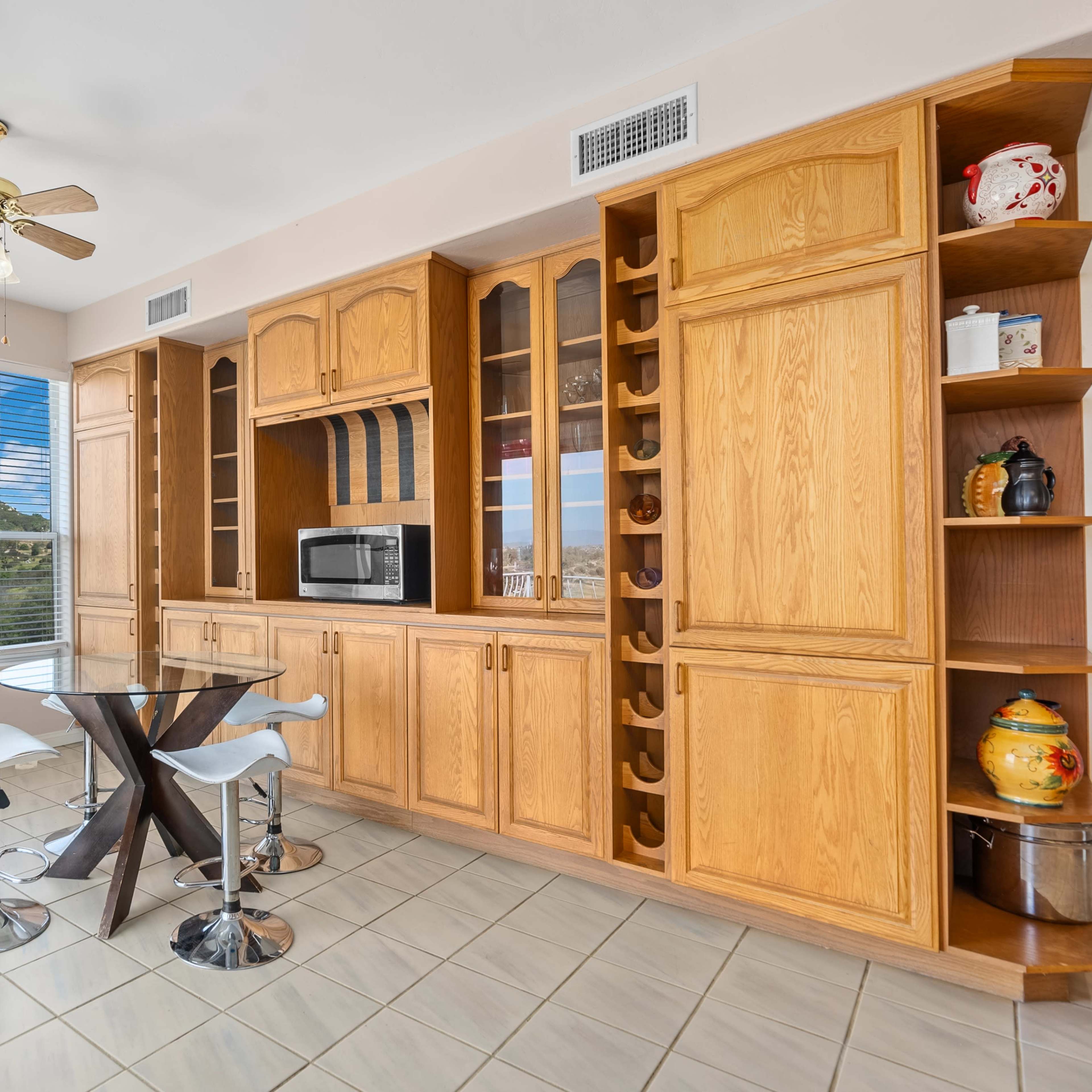 The kitchen features light wood cabinetry, a round glass dining table with modern chairs, and stainless steel appliances.