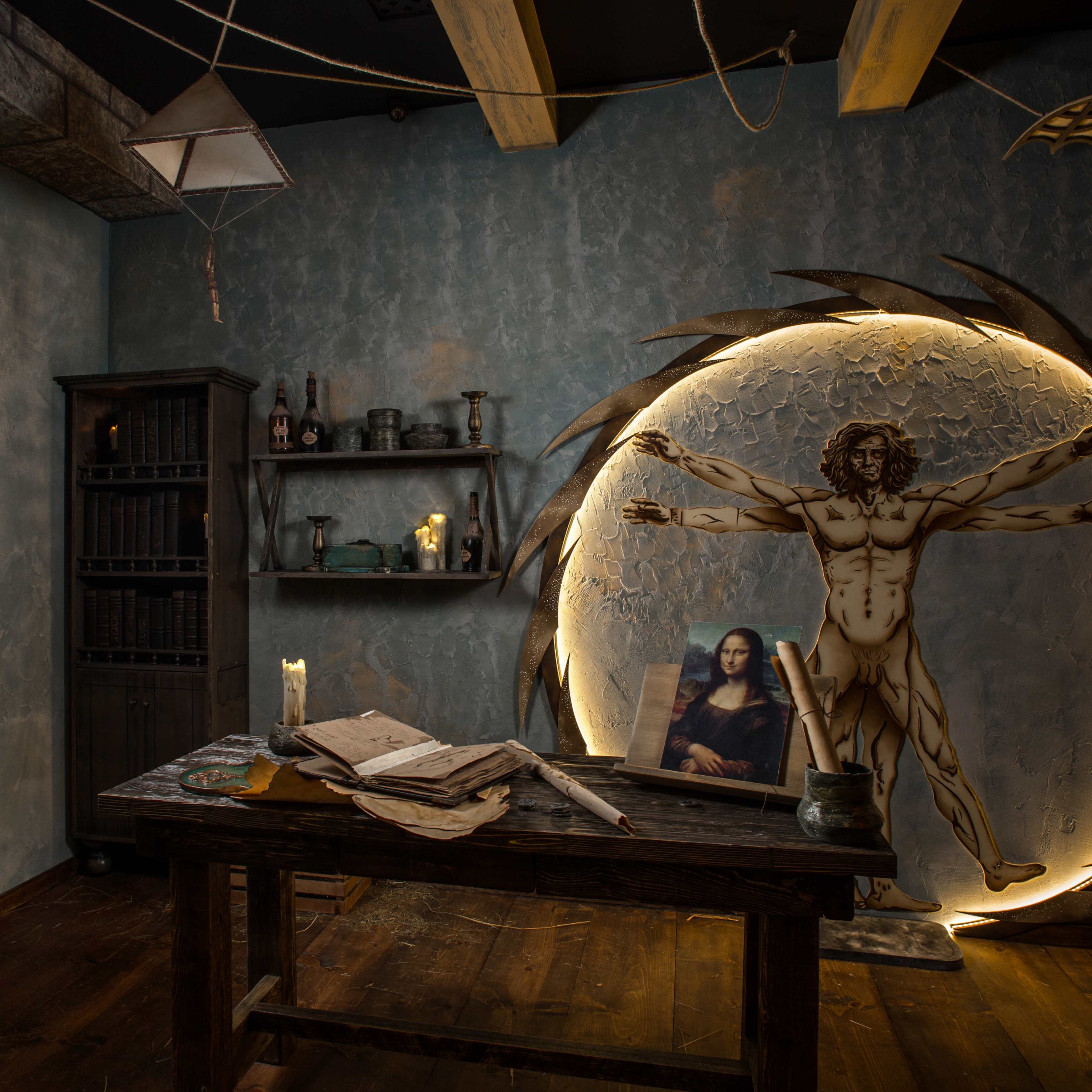 A dimly lit room with a wooden table, shelves of bottles, and a large circular artwork featuring a human figure, reminiscent of Leonardo da Vinci's Vitruvian Man, illuminated by soft light.
