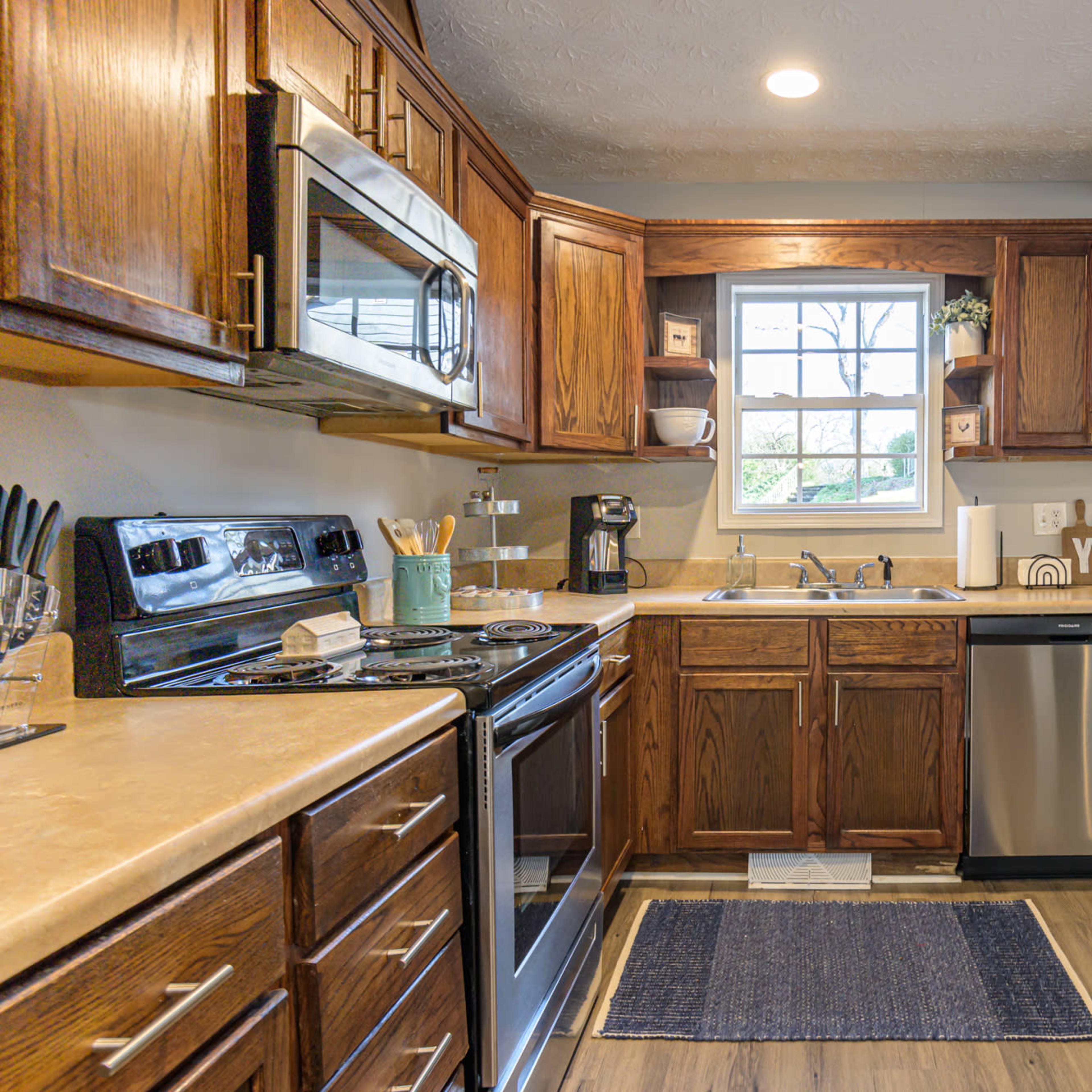 A modern kitchen features wooden cabinets, stainless steel appliances, and a small dining area with a bar stool.