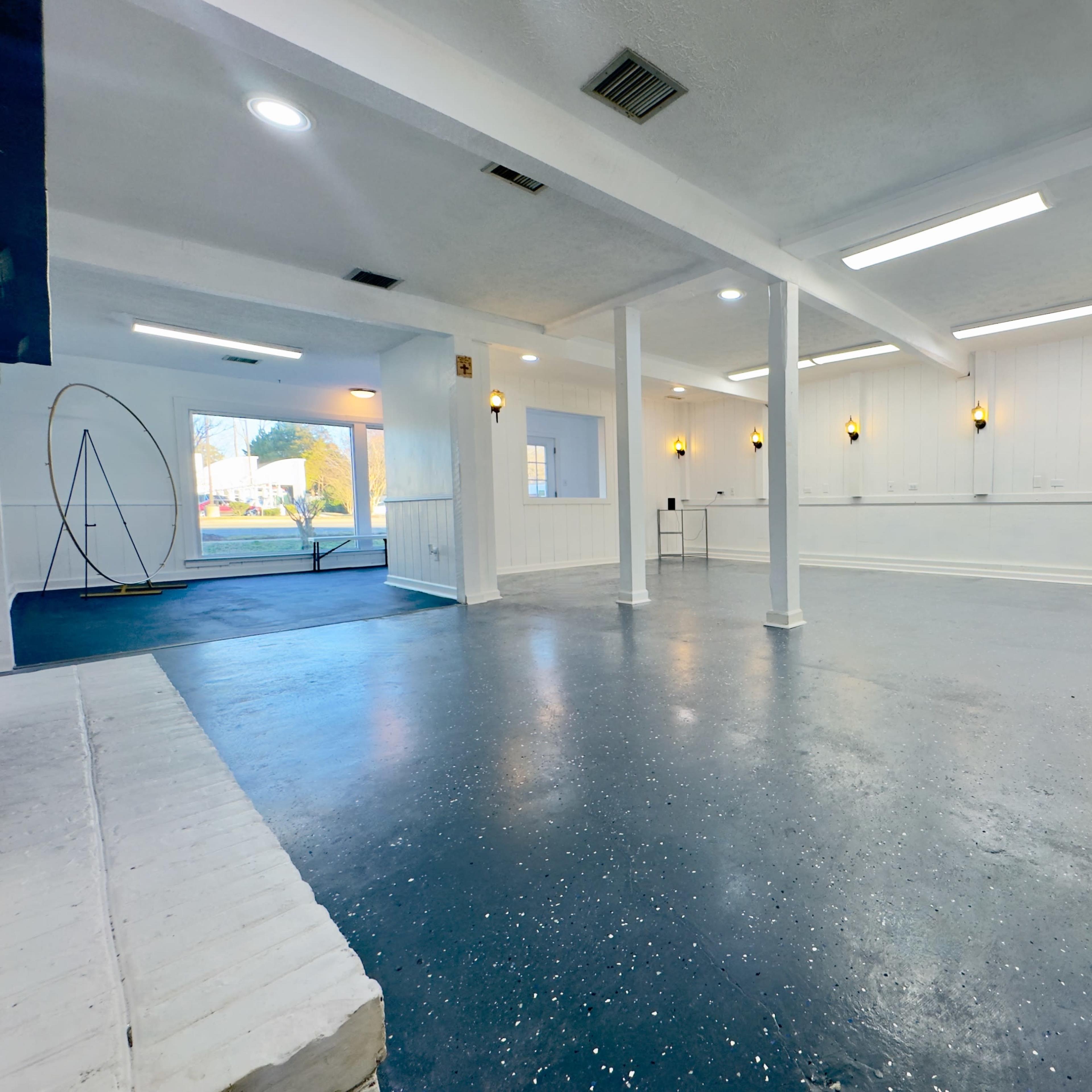 A spacious, empty room with white walls, a blue floor, and several light fixtures illuminating the area.