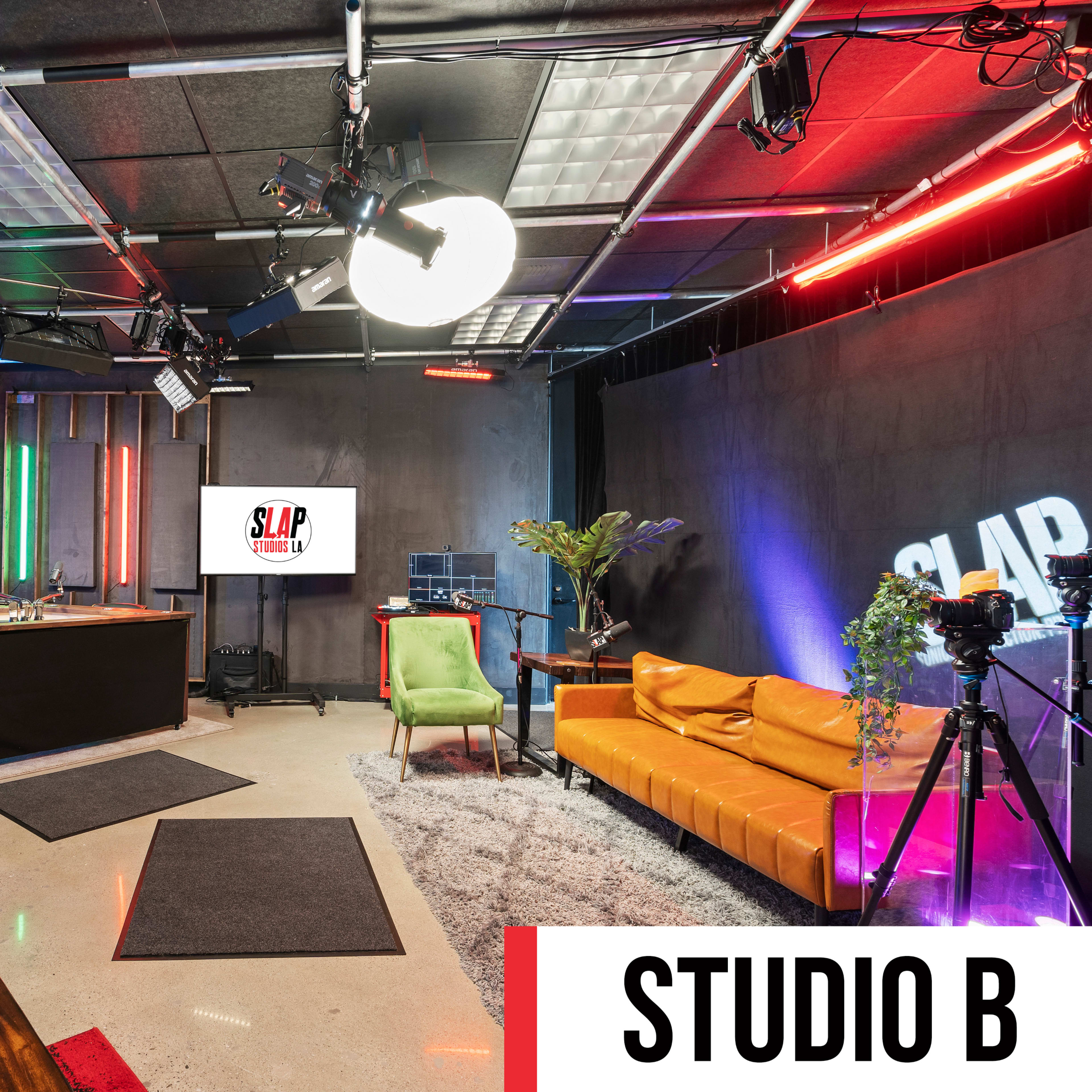 A modern multimedia studio with colorful lighting, a green couch, various plants, and a production setup including cameras and a desk.