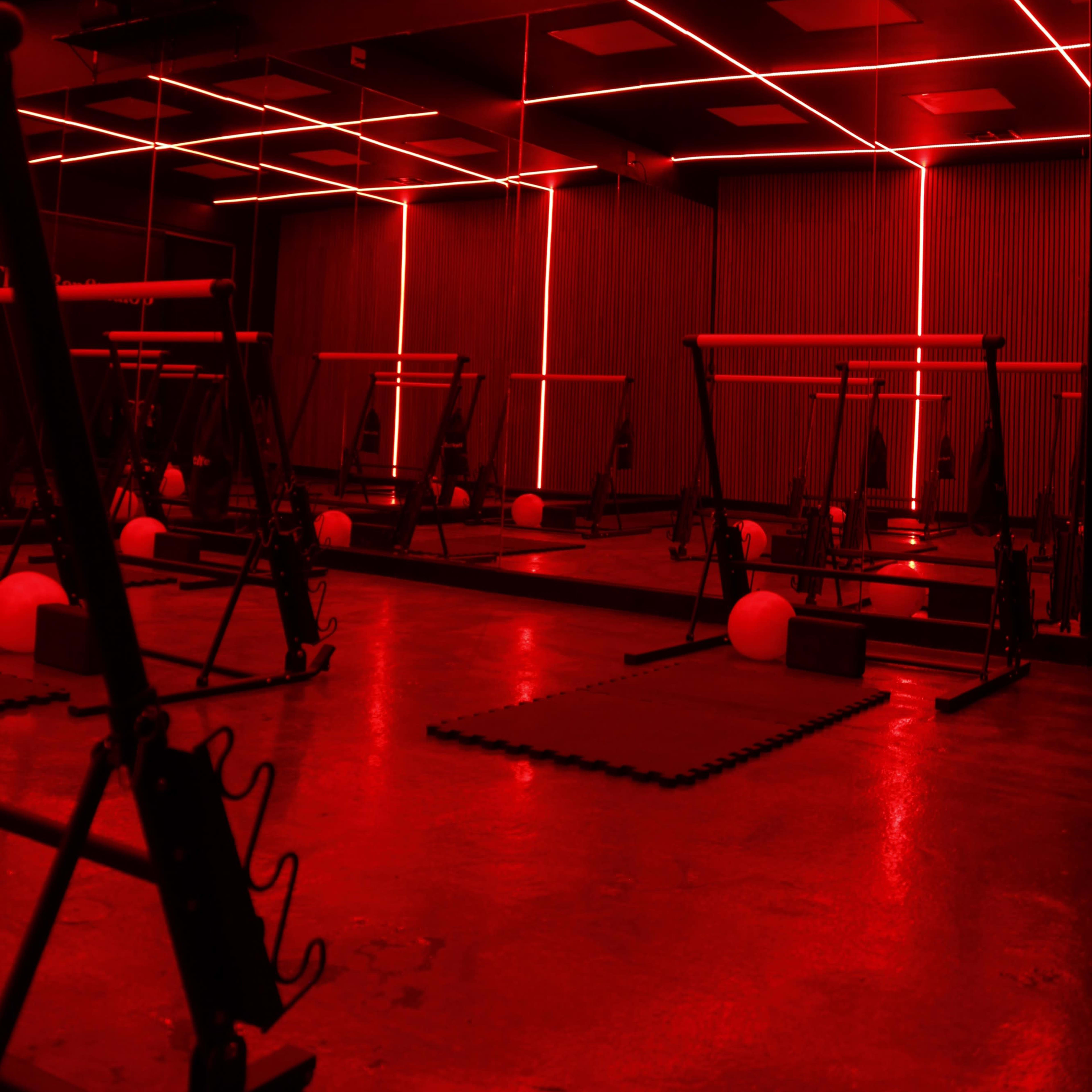 A fitness studio features exercise equipment illuminated by red neon lighting and lined with mirrors.