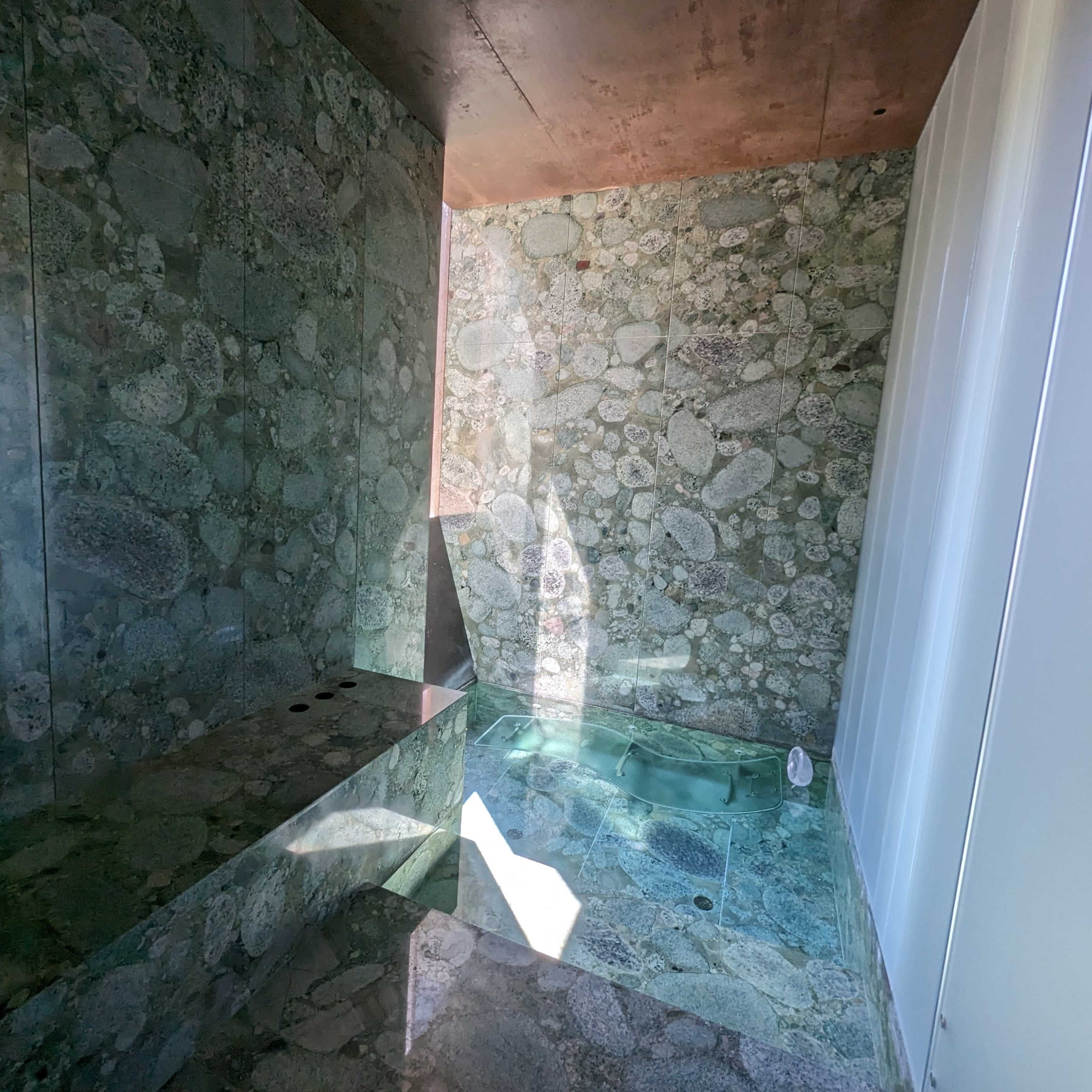 A modern shower area with textured stone walls and a small soaking tub in a corner.