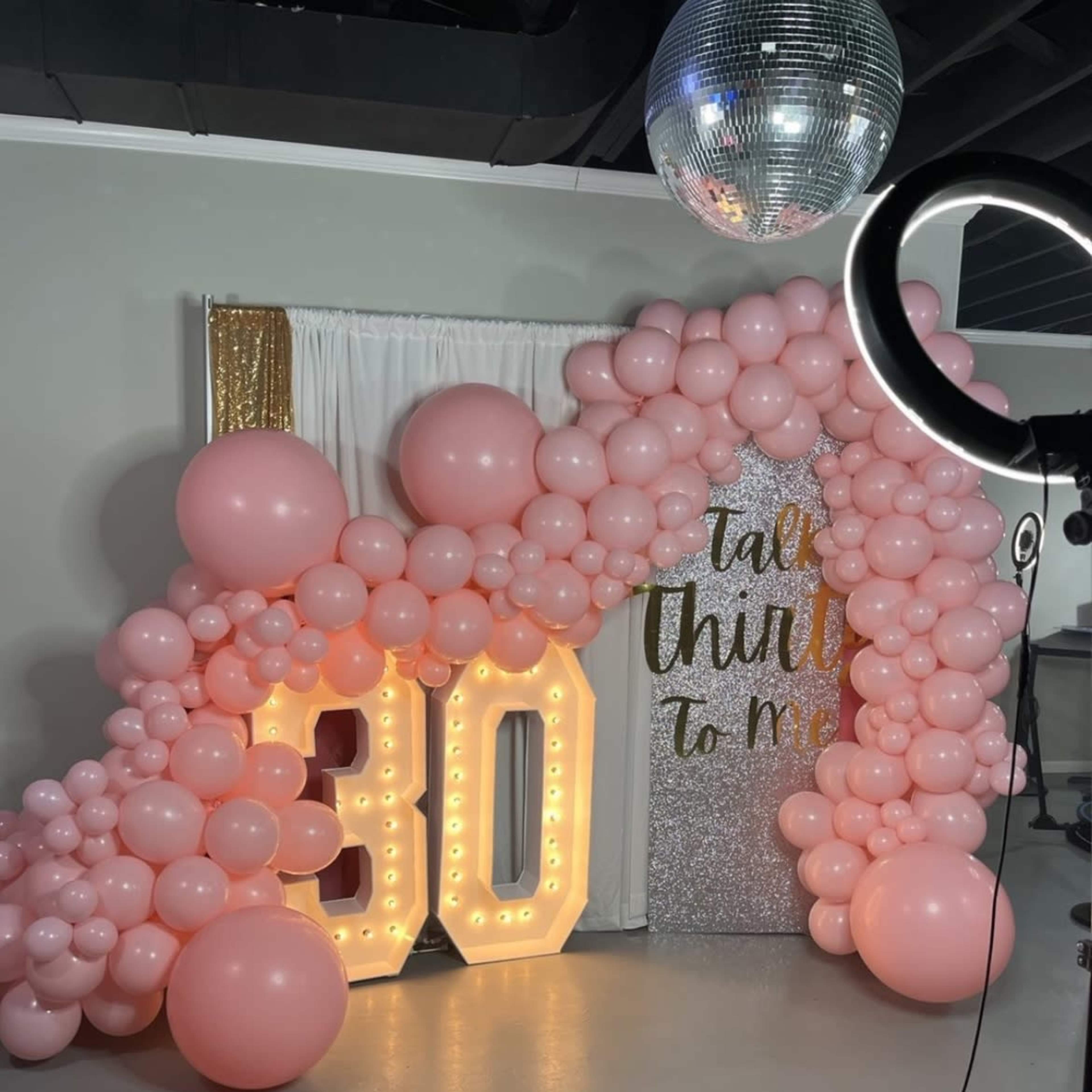 A festive backdrop featuring large illuminated numbers "30" surrounded by pink balloons and a glittery panel with the text "Talk thirty to me."