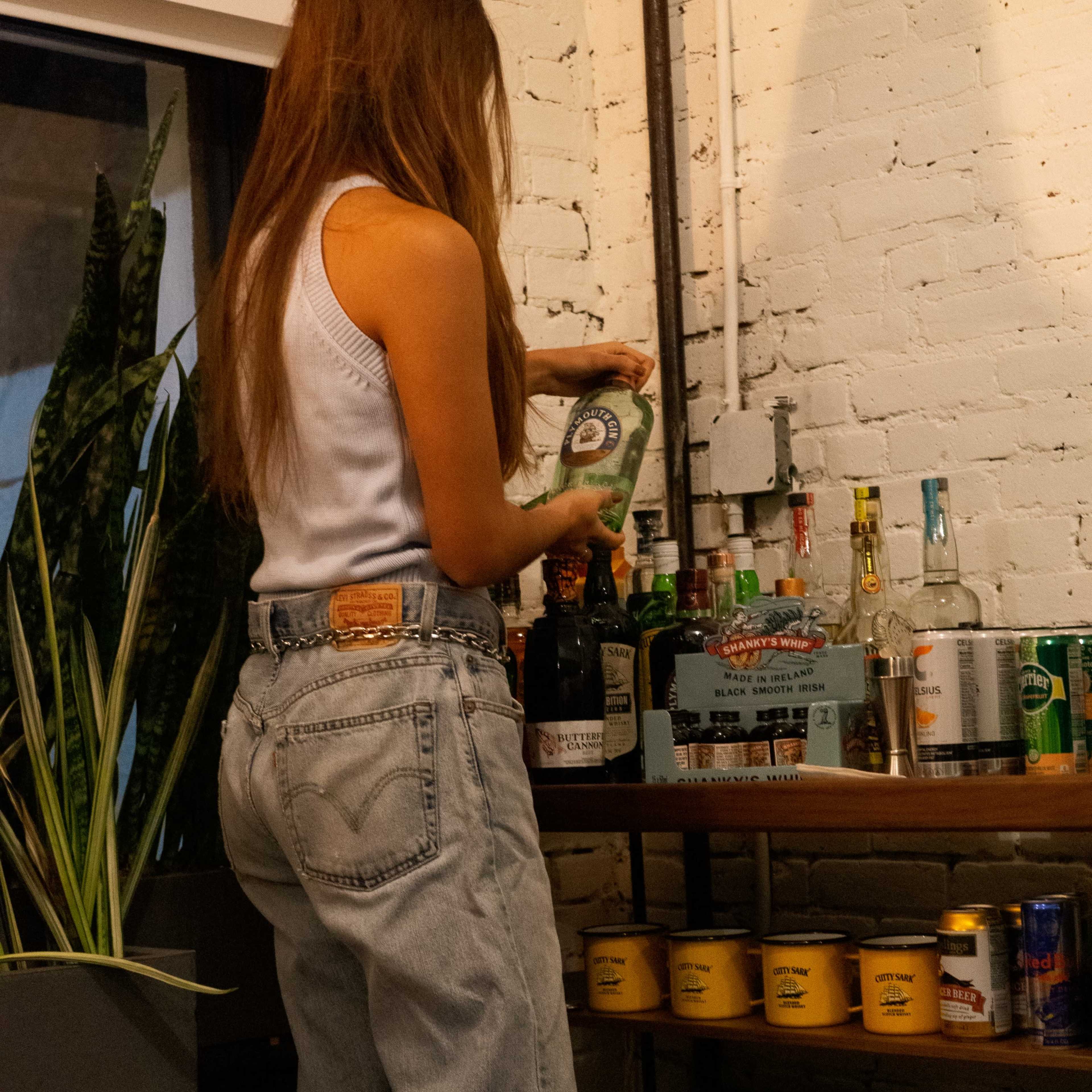 A person stands in front of a shelf, placing a bottle on a collection of various alcoholic beverages and mixers.