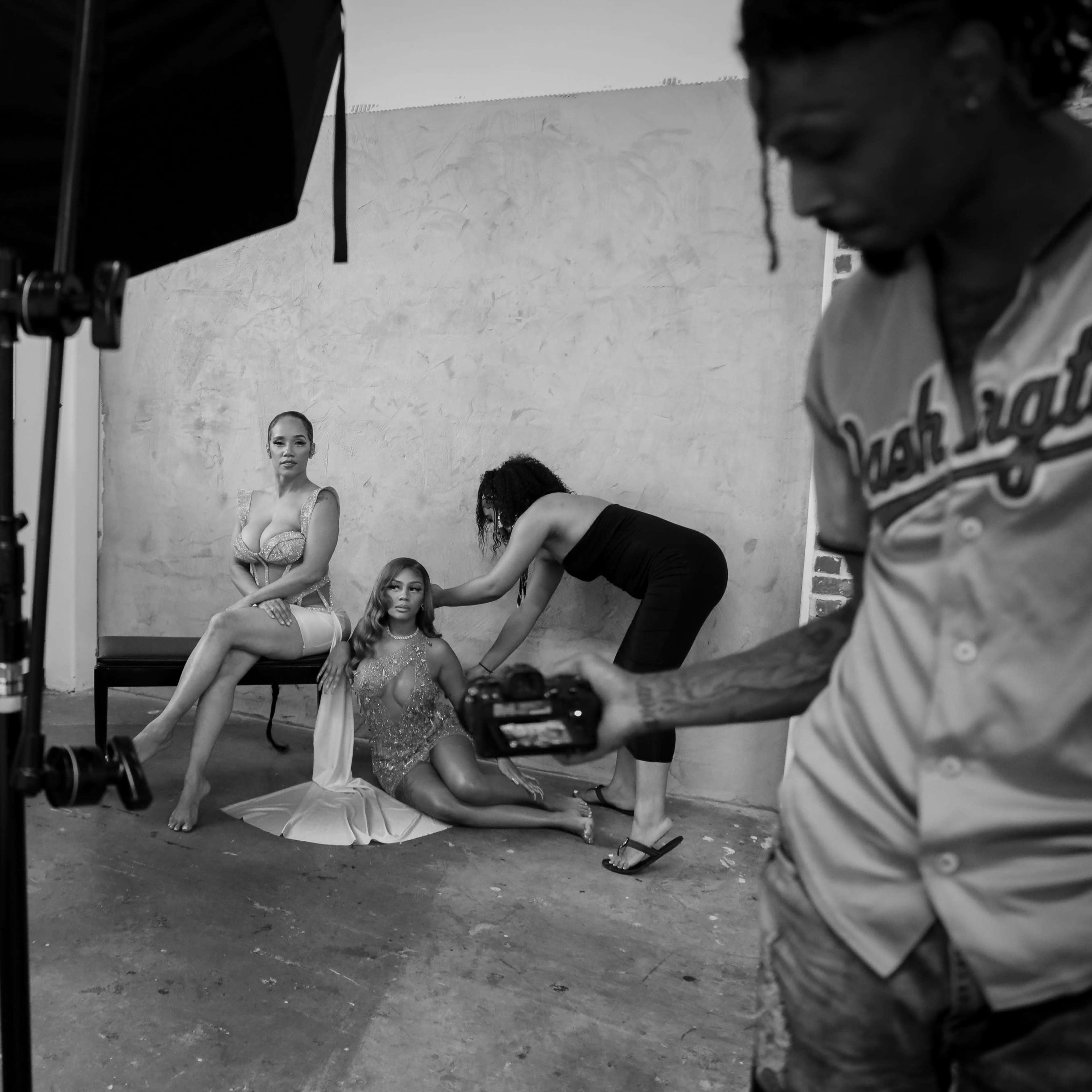 A photoshoot is taking place in a studio with two models posing while a stylist adjusts the hair of one model.