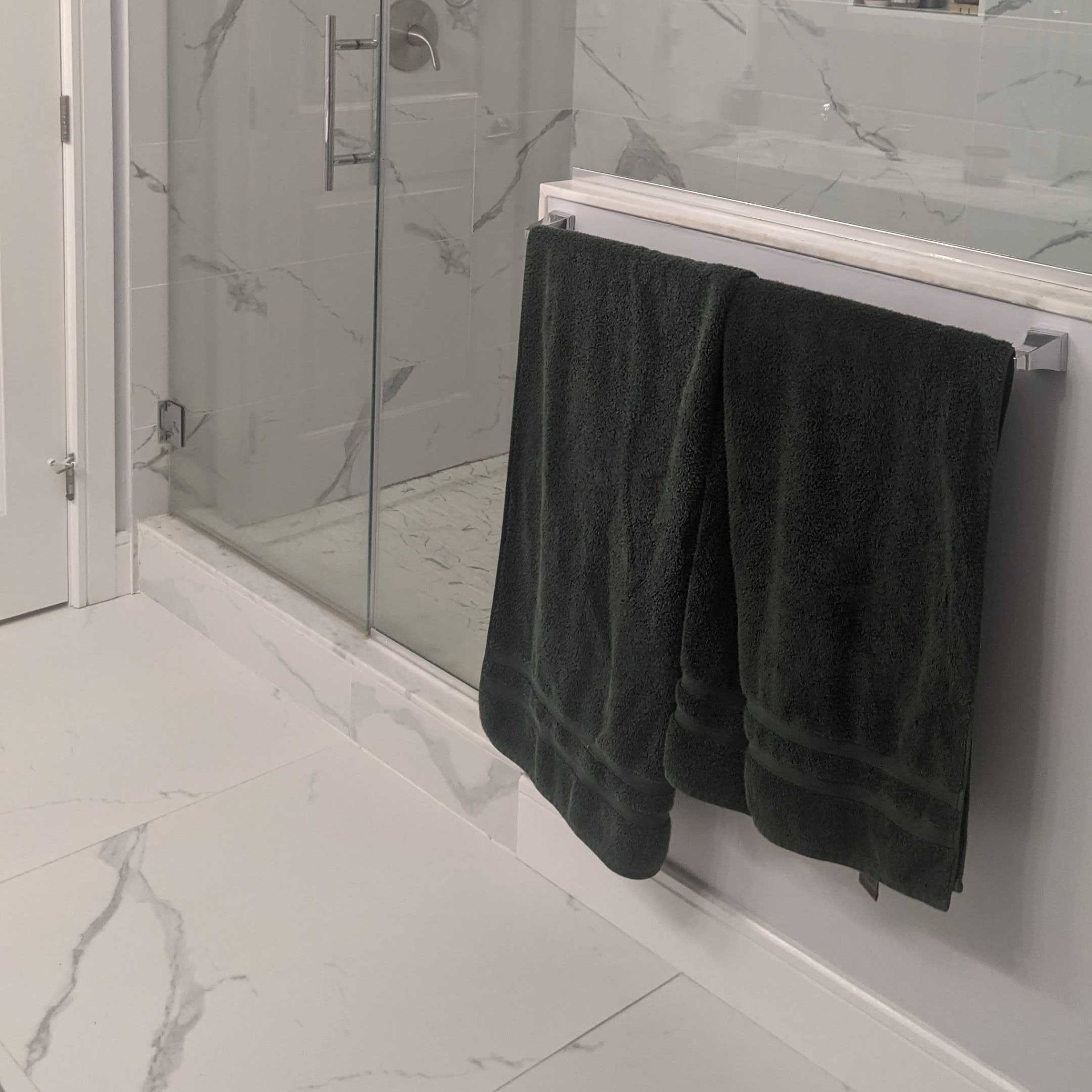 A modern bathroom featuring a glass shower enclosure, a white vanity with a mirror, and two hanging dark green towels.