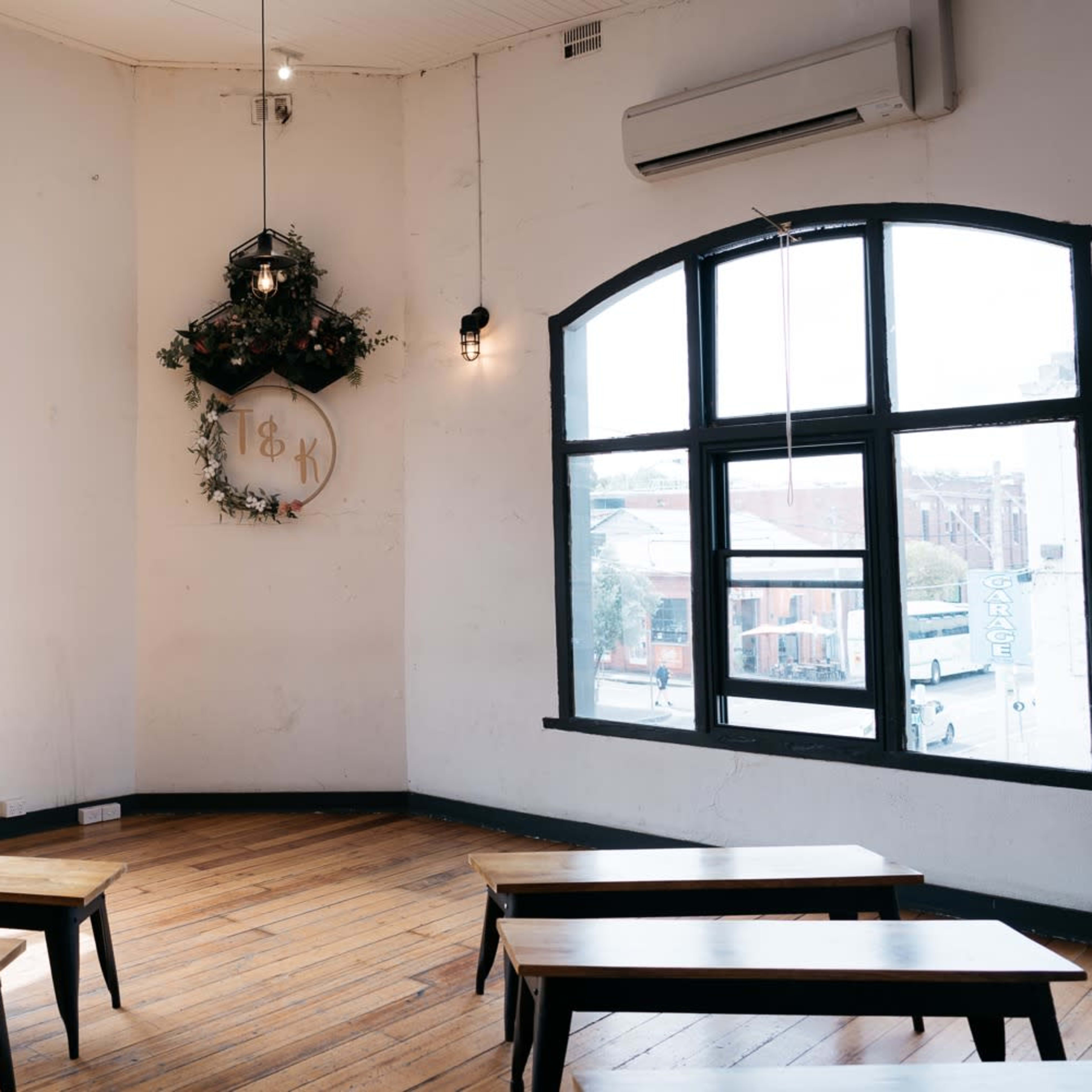 A corner of a room with wooden benches arranged in front of large windows, featuring a decorative wall with a circular emblem and greenery.