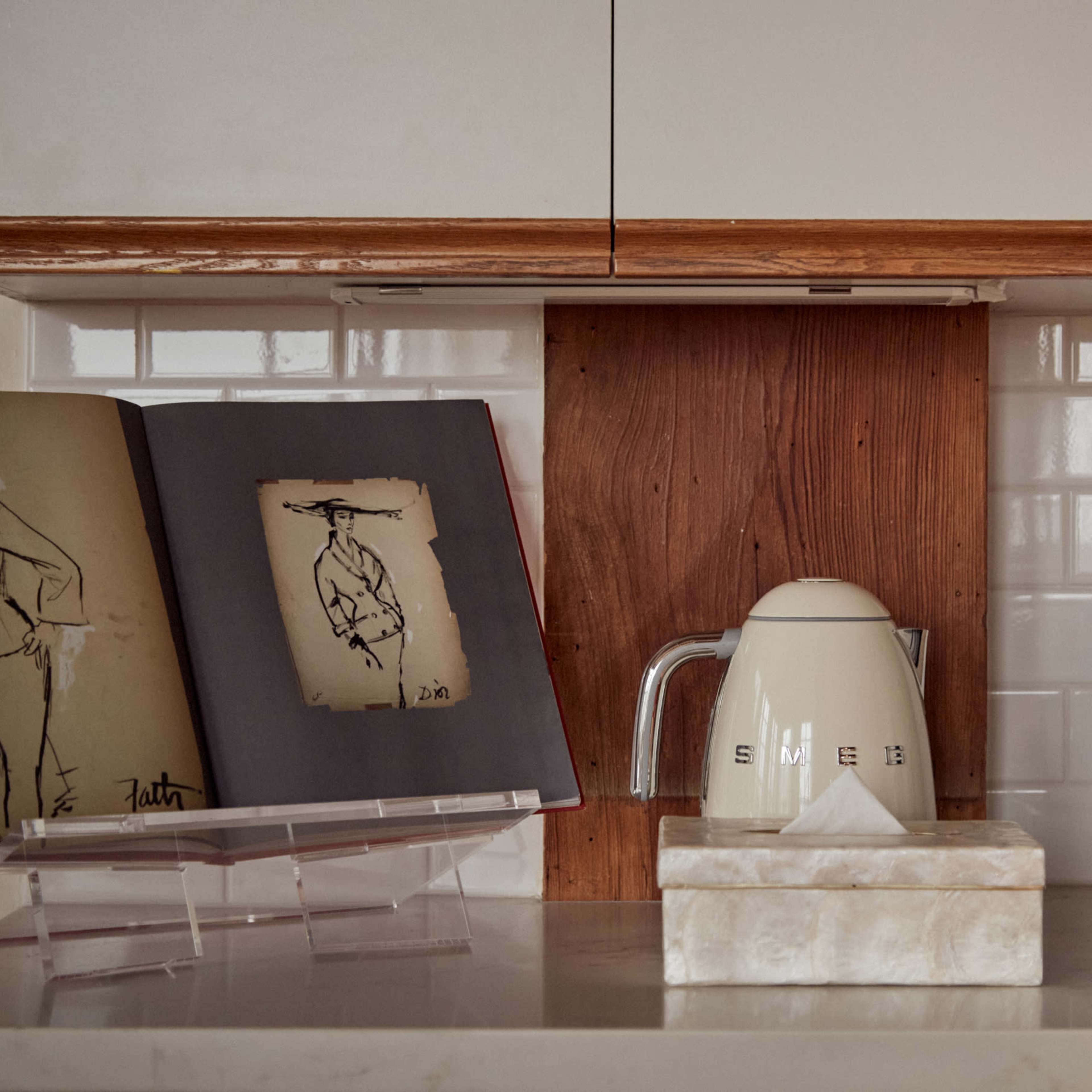 A kitchen countertop featuring a kettle, stoneware container, and a decorative book stand displaying artworks.