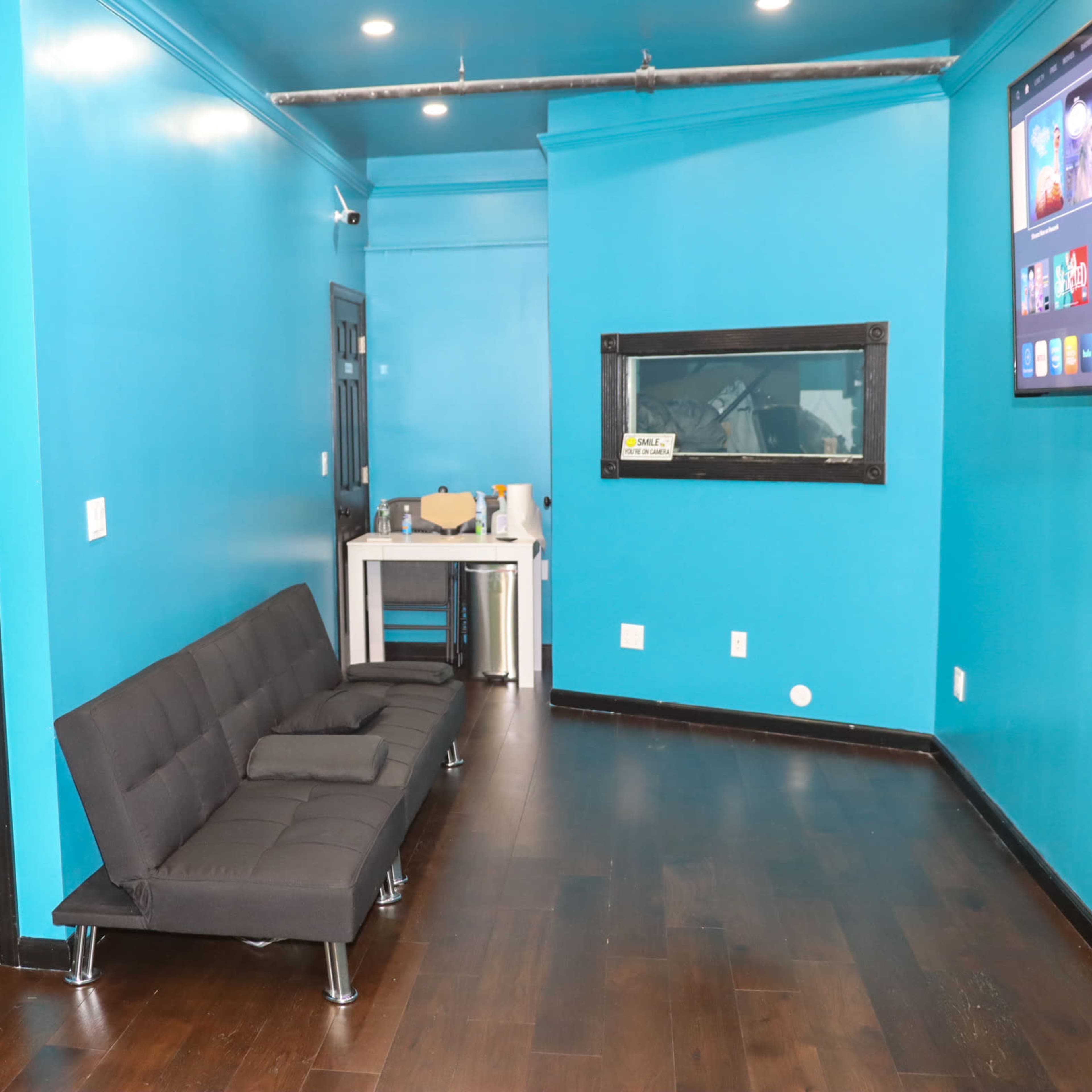 The room features a bright turquoise wall, a black door with a coat rack, a black sofa, and a television mounted on the wall.