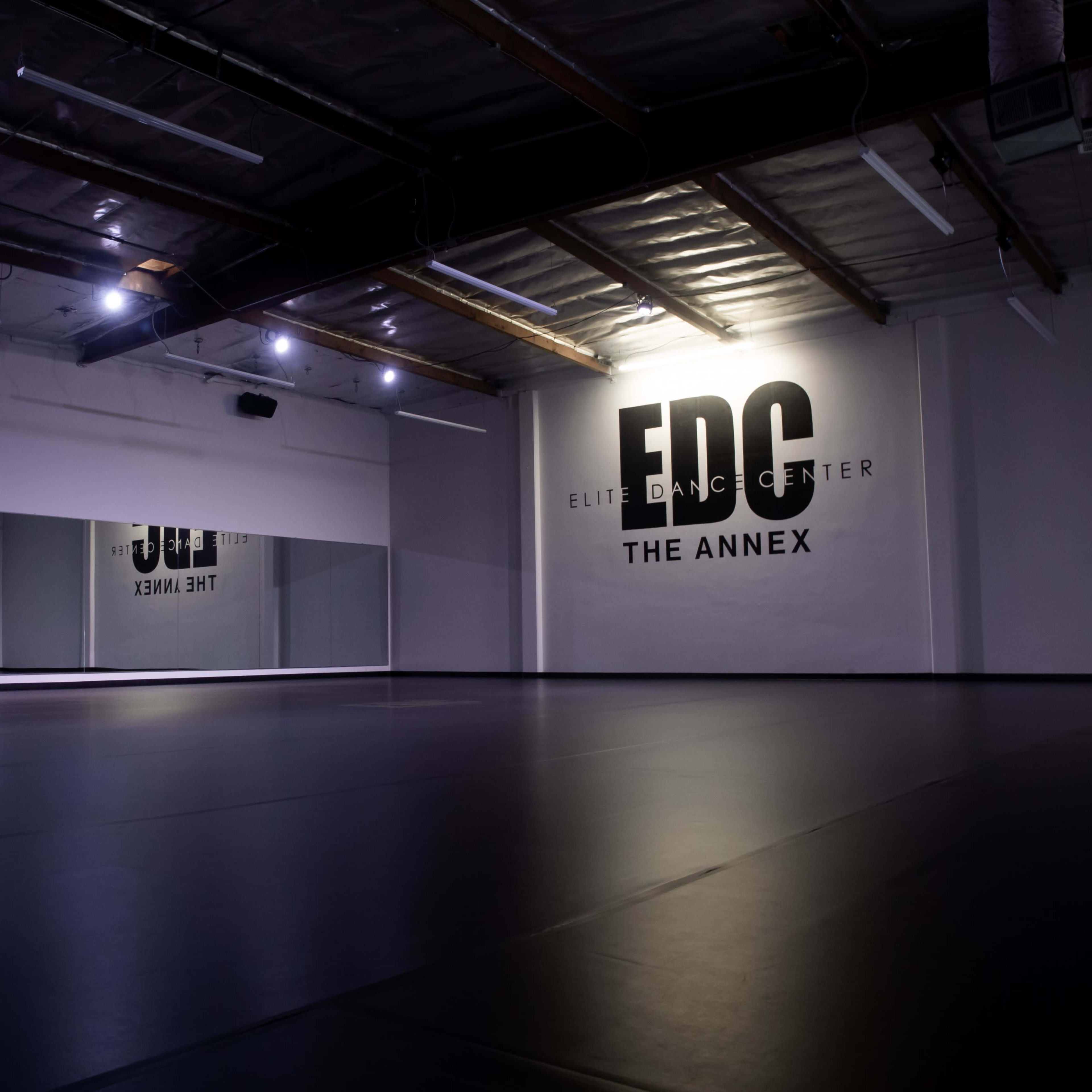 An empty dance studio features a mirrored wall and a large logo on the back wall.