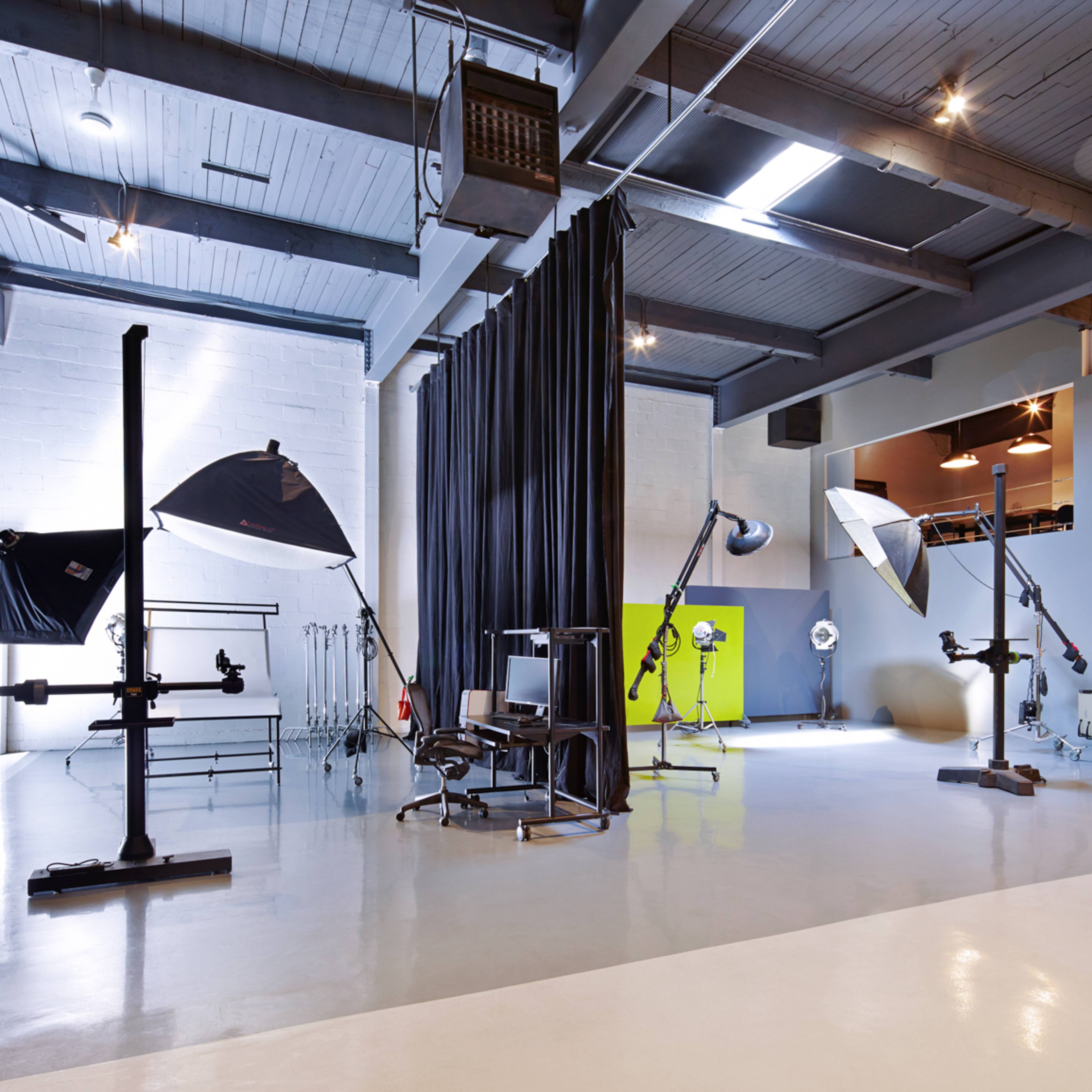 A spacious photography studio with various lighting setups, a chair, and a backdrop curtain.