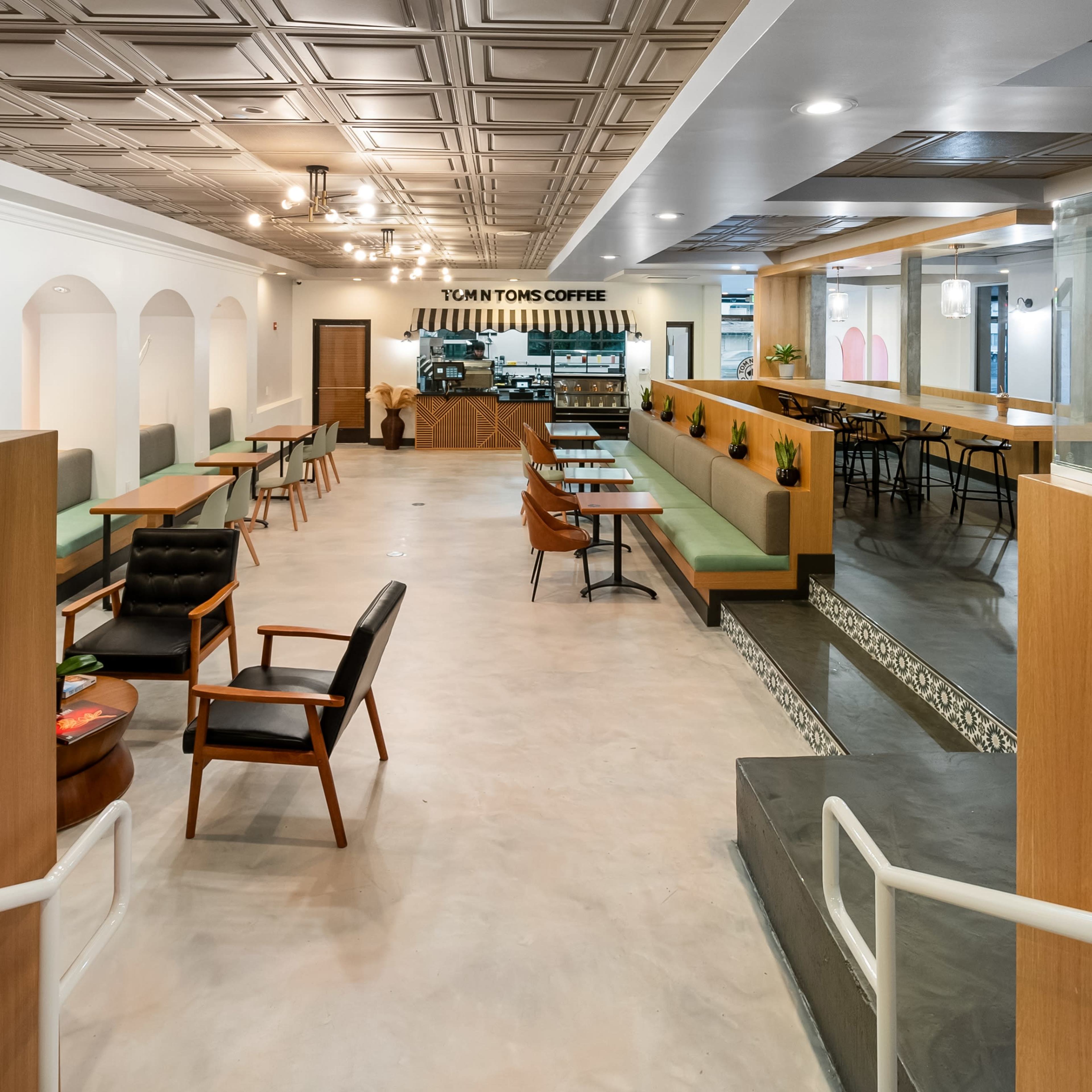 A modern coffee shop interior with wooden seating arrangements, tables, and a counter in the background.