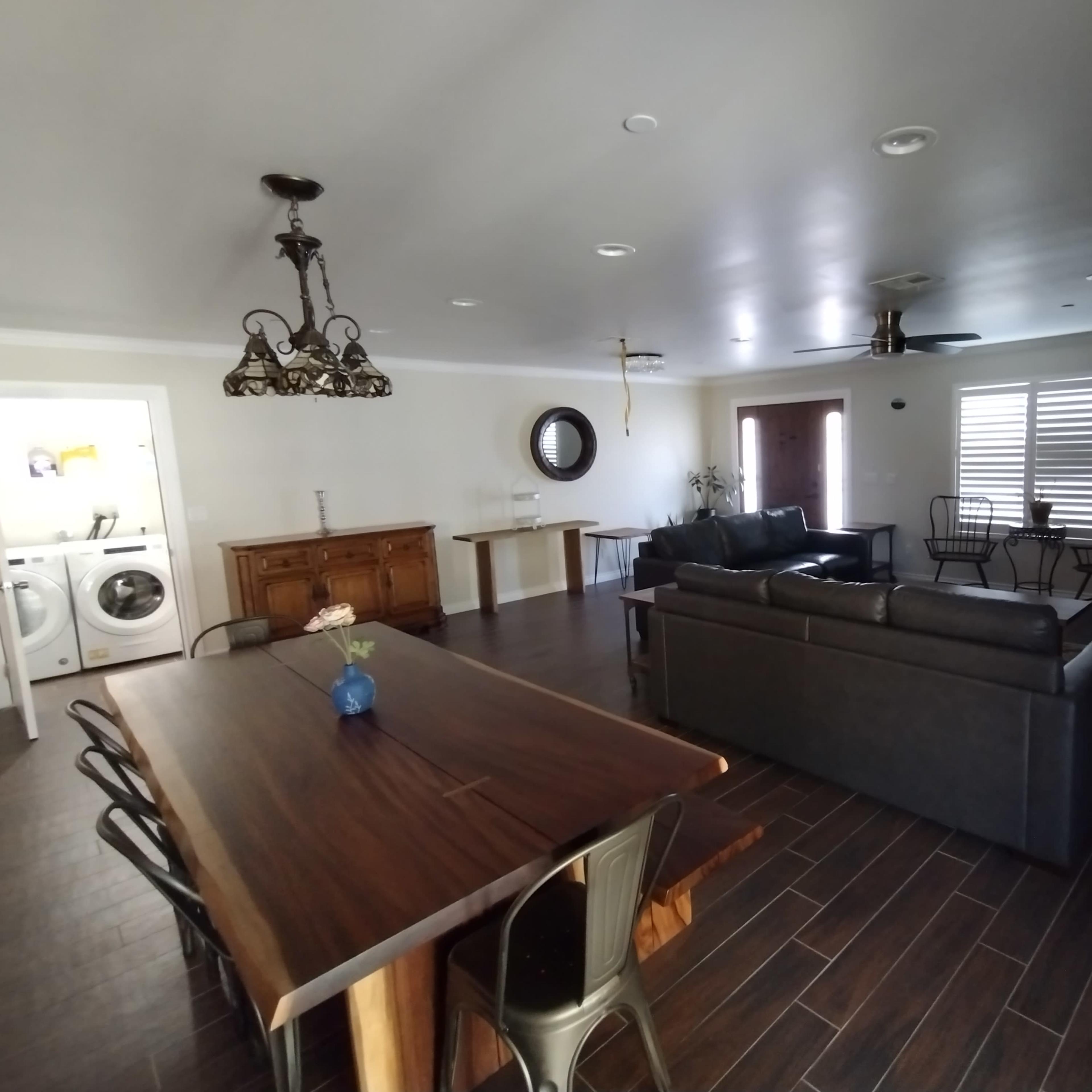 A spacious living area with a dining table, a sofa, and a laundry room visible in the background.