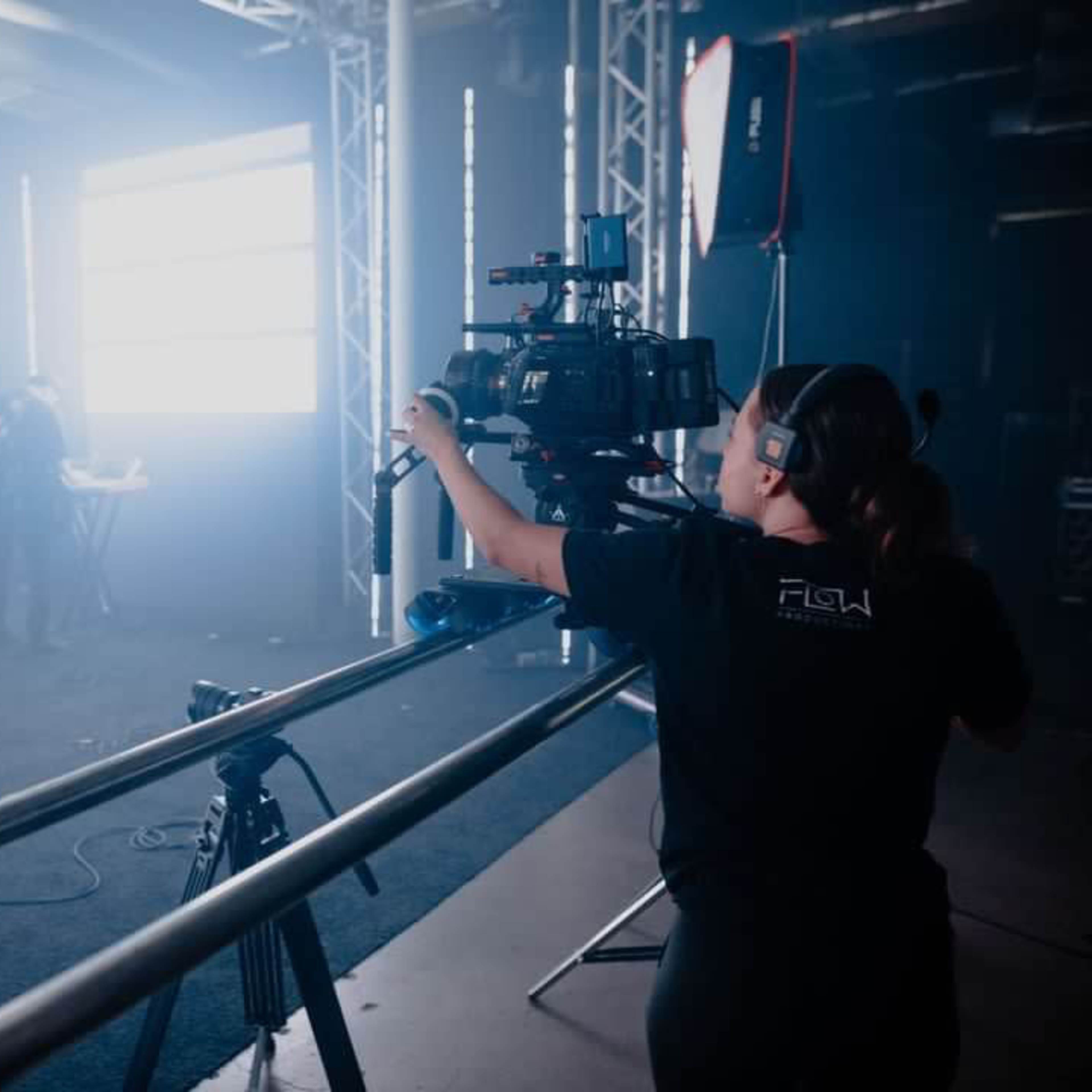 A camera operator films a musician performing on stage while a band is set up in the background.