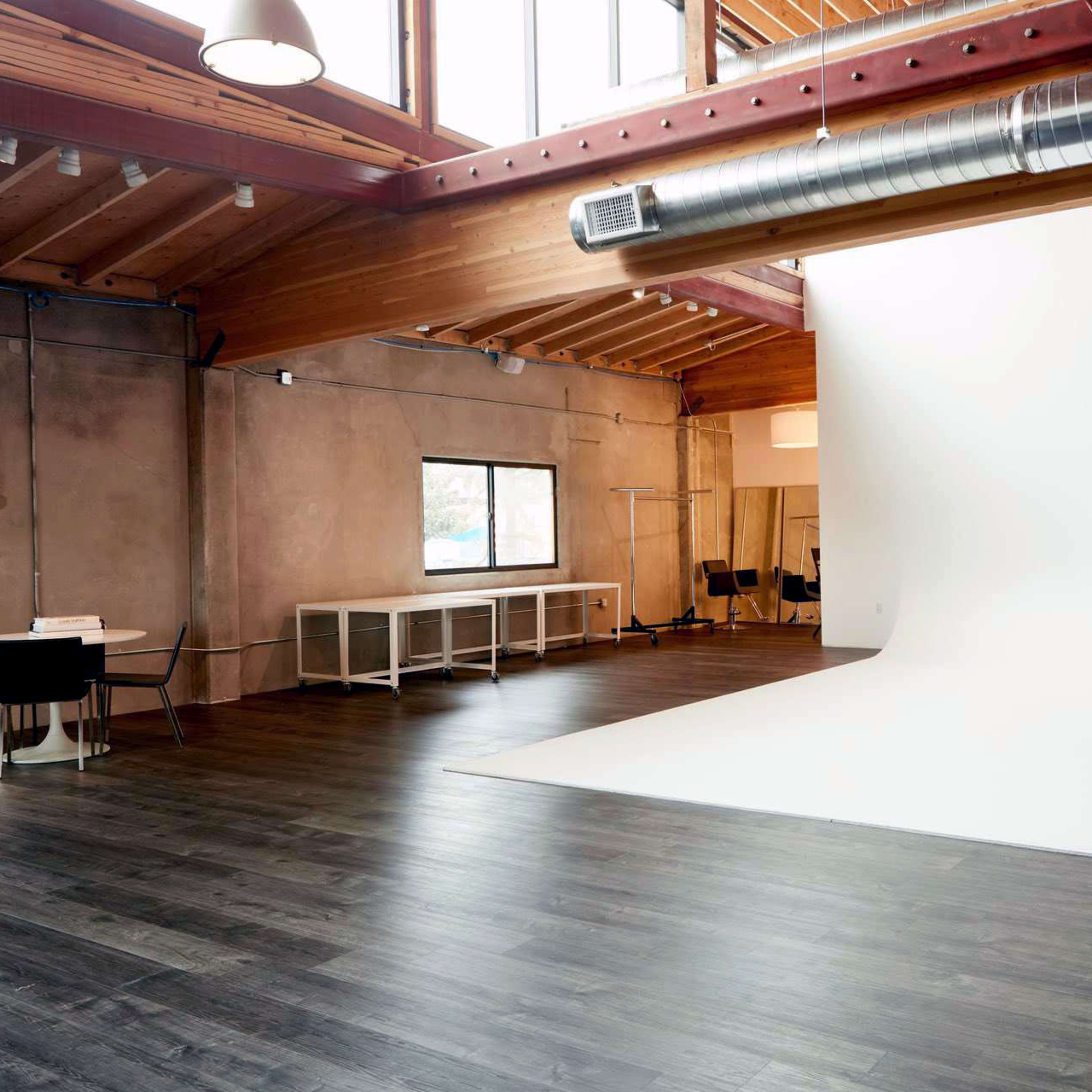A spacious studio with wooden beams, a large white backdrop, and a seating area with a table and chairs.