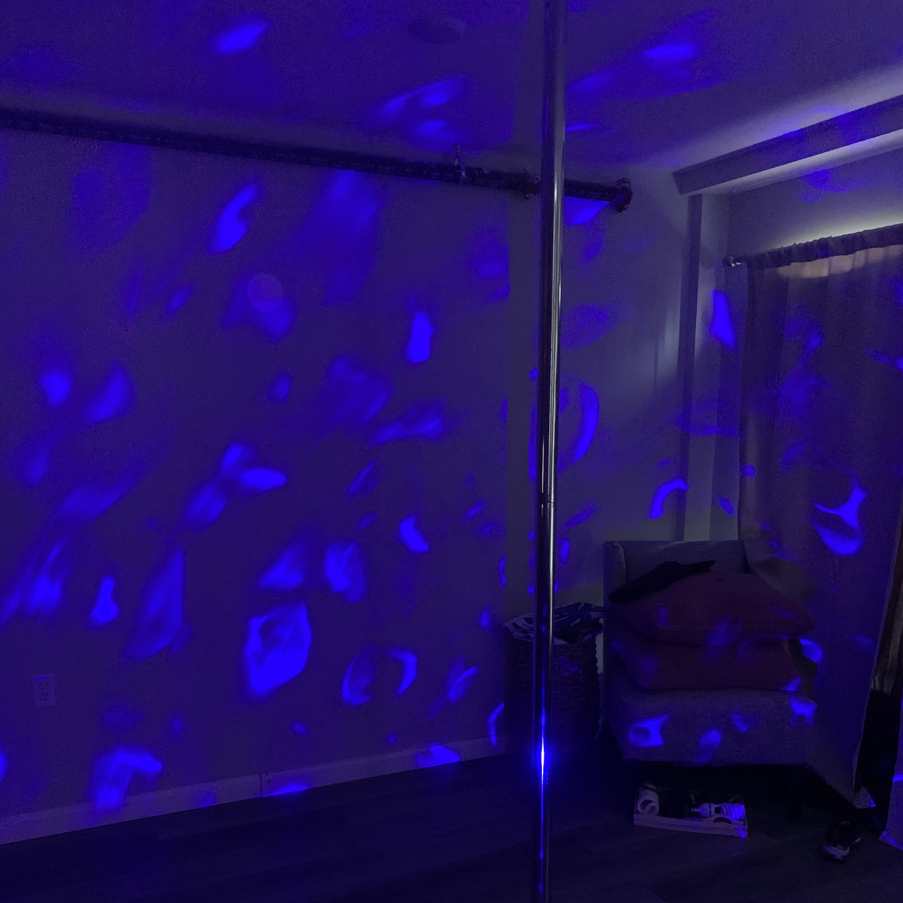 A dimly lit room with a stainless steel pole and blue lights projecting patterns on the walls and floor.