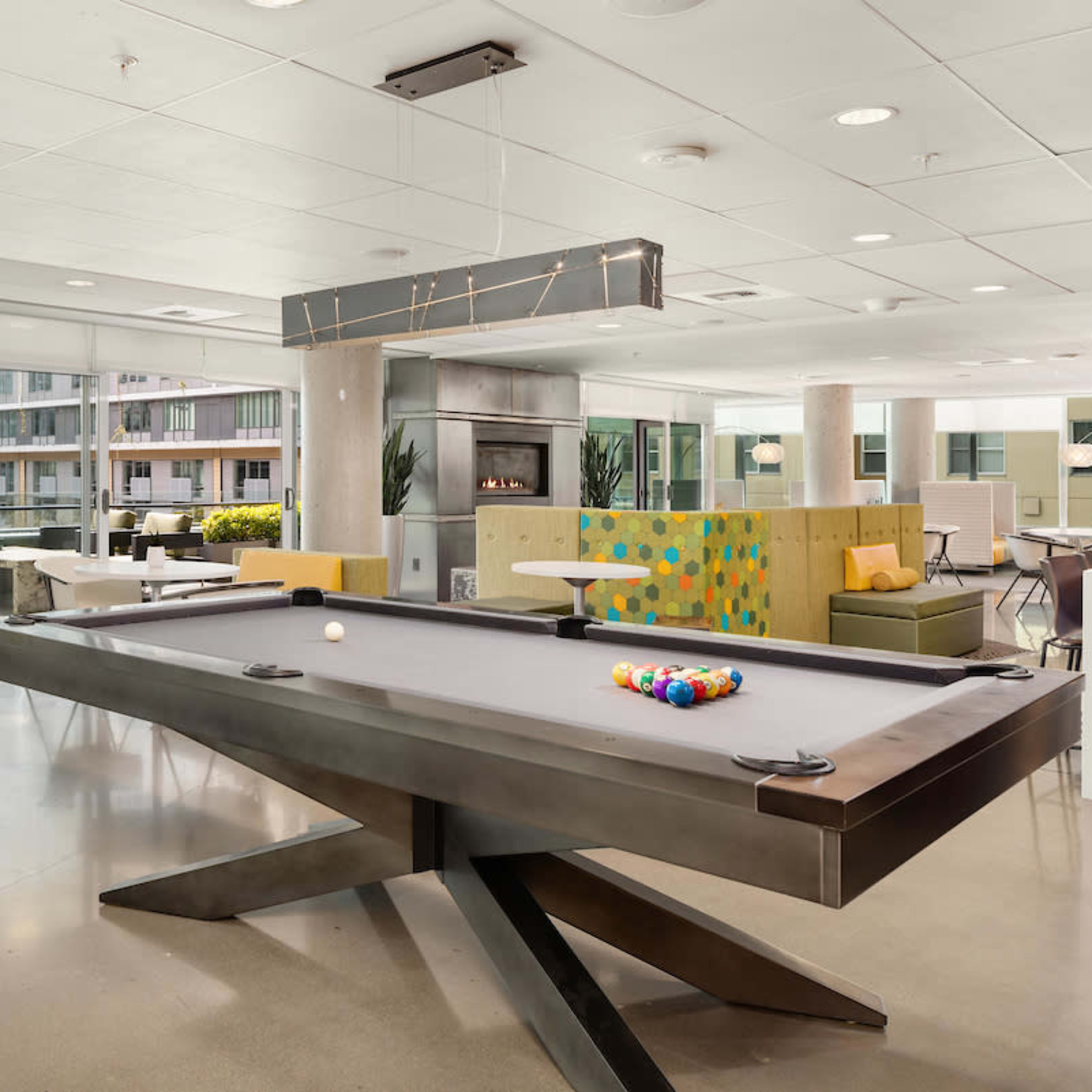 A modern common area with a billiards table, lounge seating, and large windows overlooking an outdoor space.