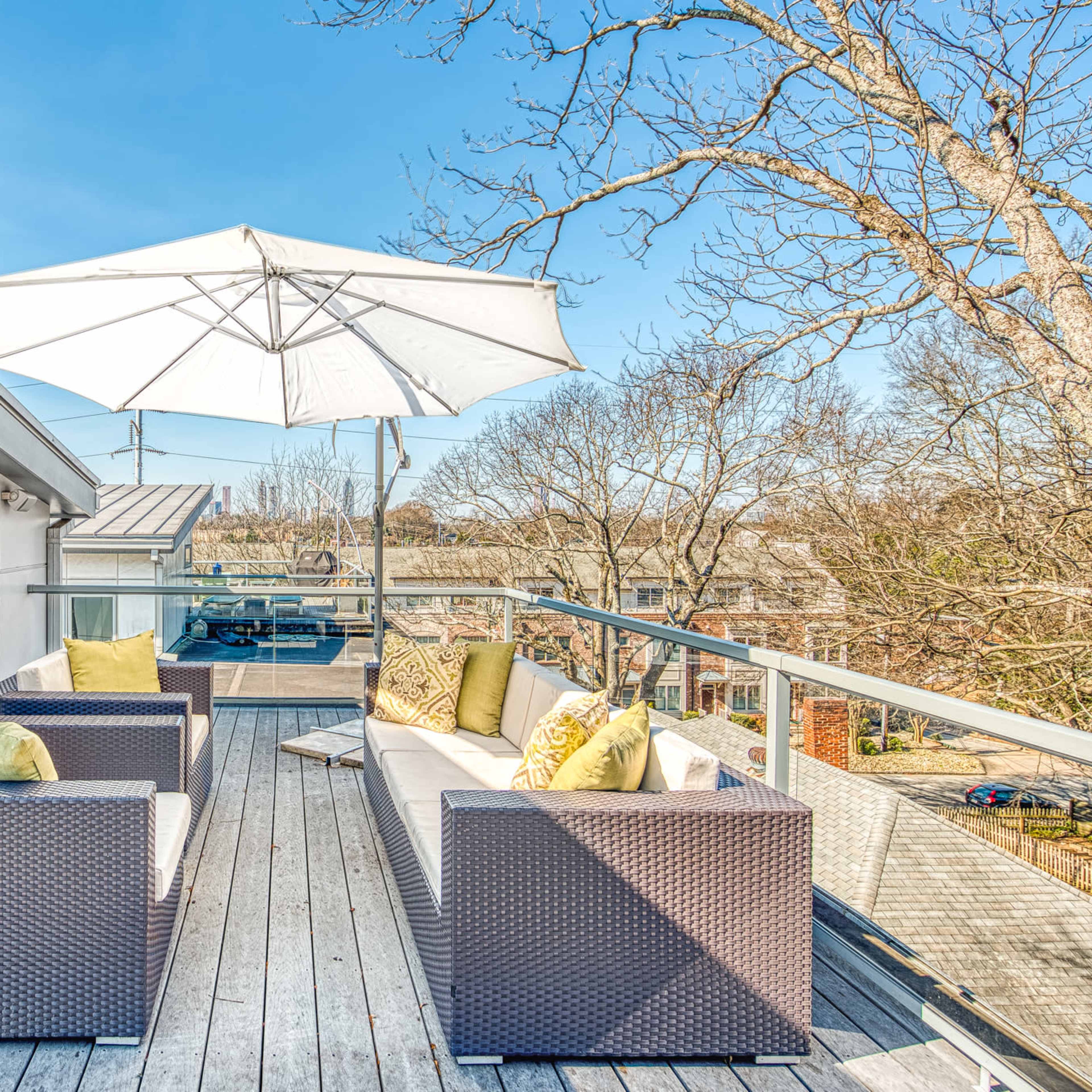A rooftop patio features two wicker sofas with green and yellow cushions beneath a large white umbrella.