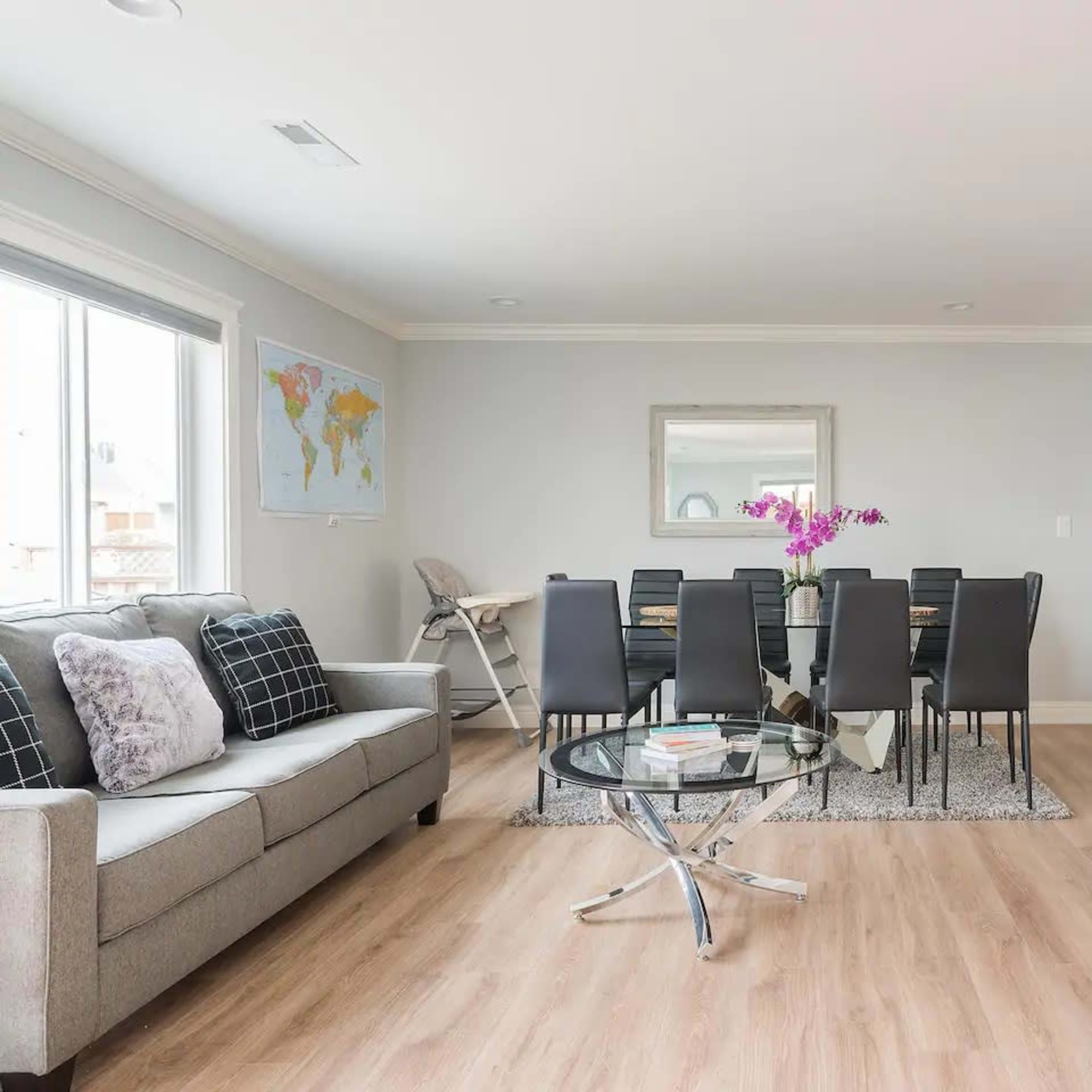 A modern living room features a gray sofa, a glass coffee table, and a dining area with a large table surrounded by black chairs.
