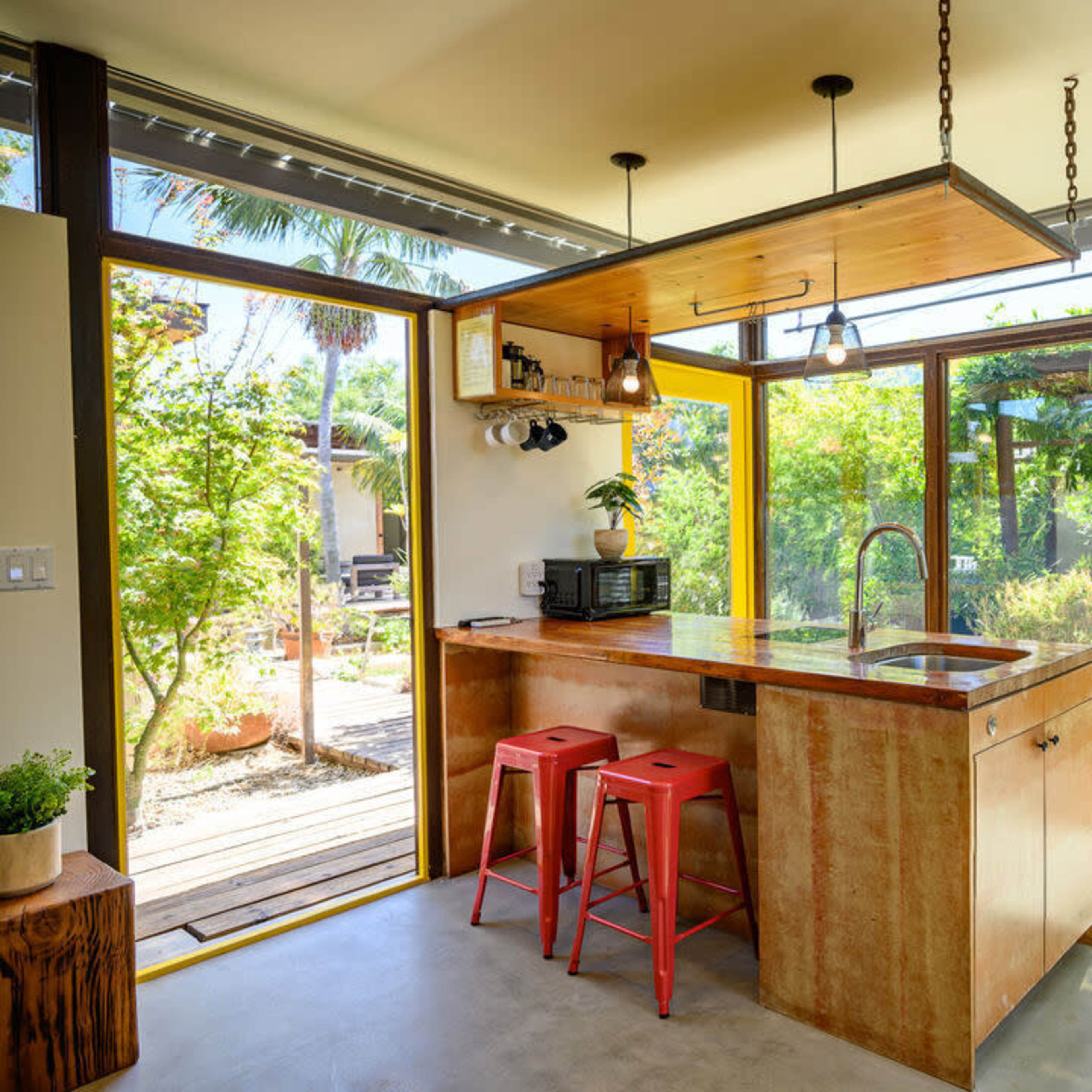 A modern kitchen with a wooden island, red stools, and large windows overlooking a garden.