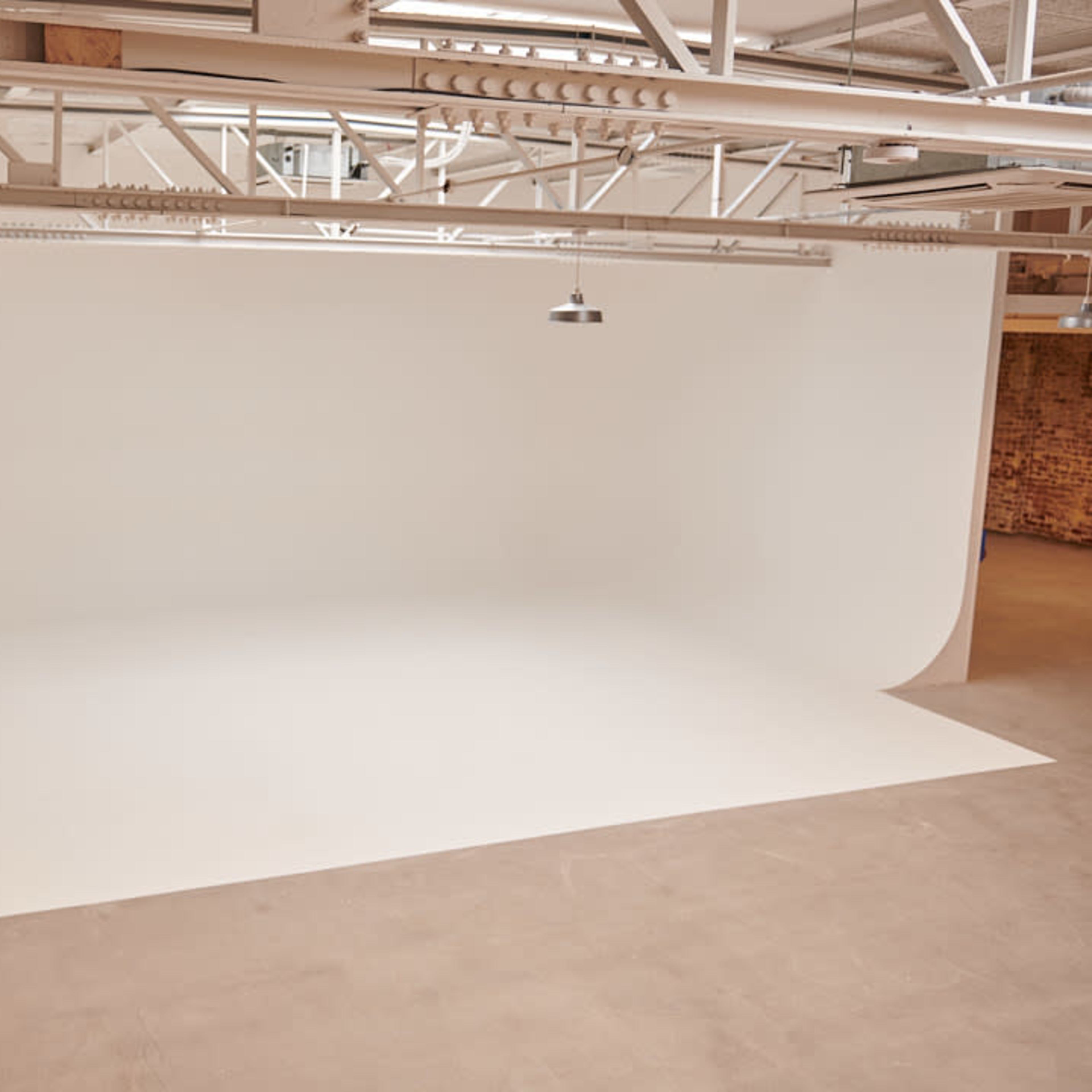 A spacious studio with a seamless white backdrop and industrial-style lighting overhead.