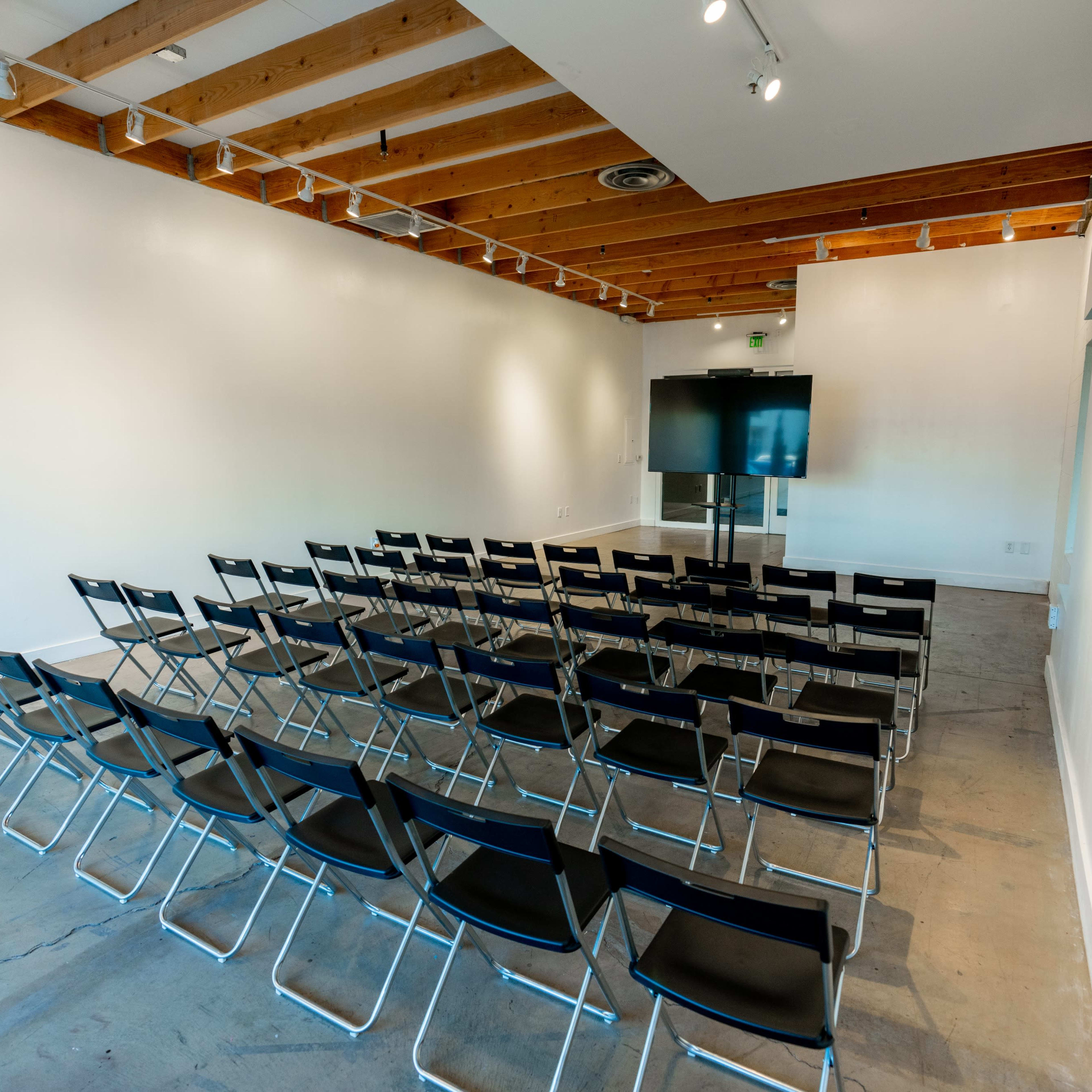 A conference room features rows of black chairs facing a large screen against a white wall.