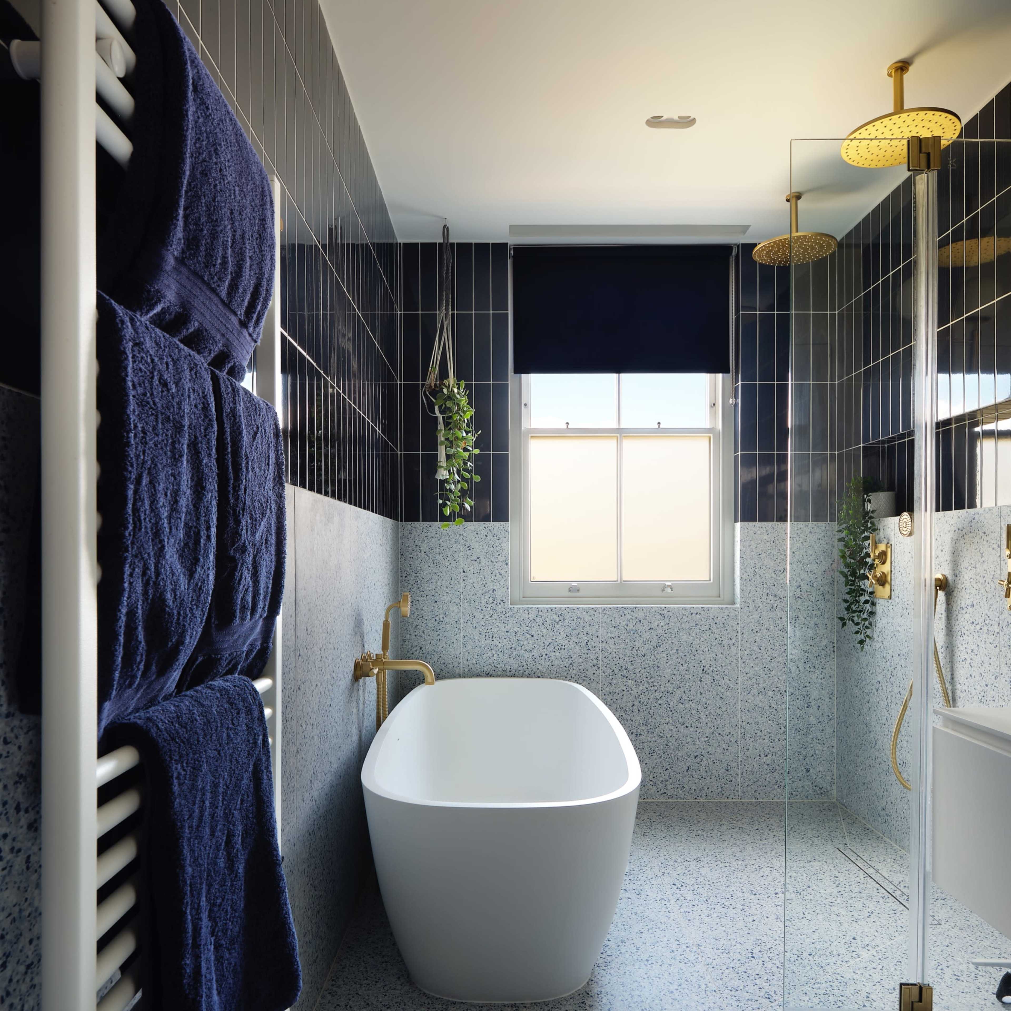 The bathroom features a freestanding white tub, a glass shower enclosure, and navy blue towels hanging on a heated towel rack against tiled walls.