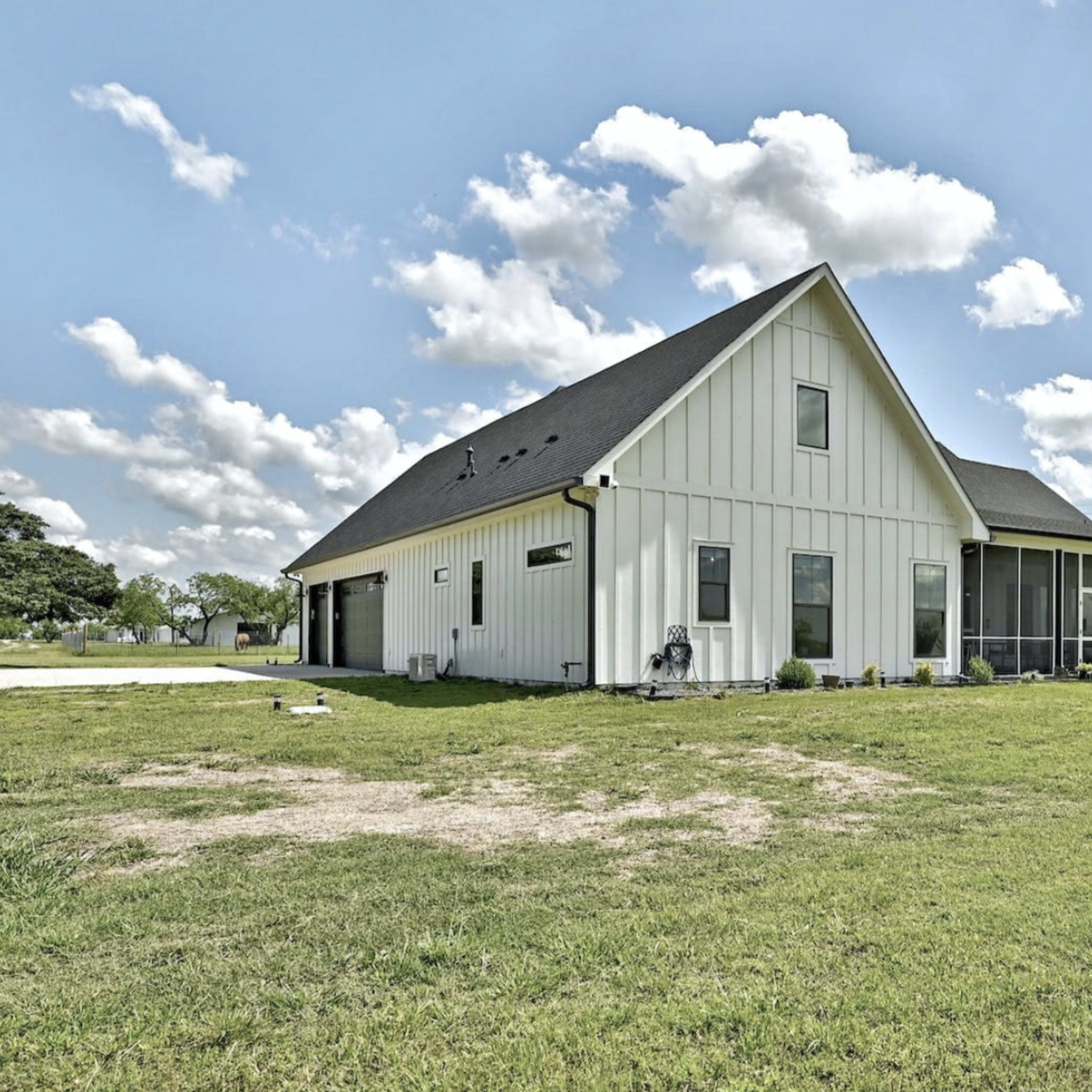 A modern white house with a sloped roof is surrounded by green grass and trees under a partly cloudy sky.