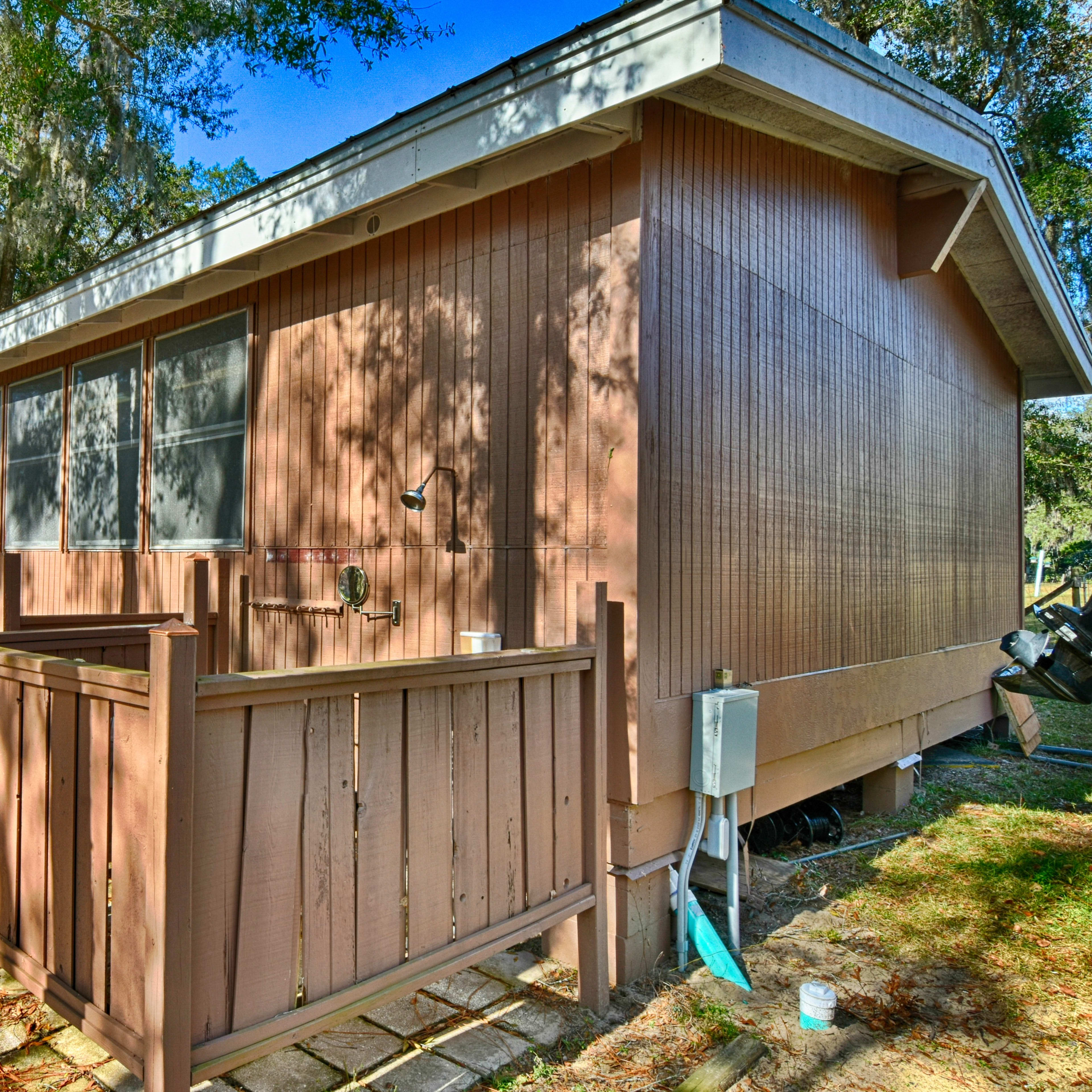 The side of a wooden cabin with a small deck and surrounded by trees.